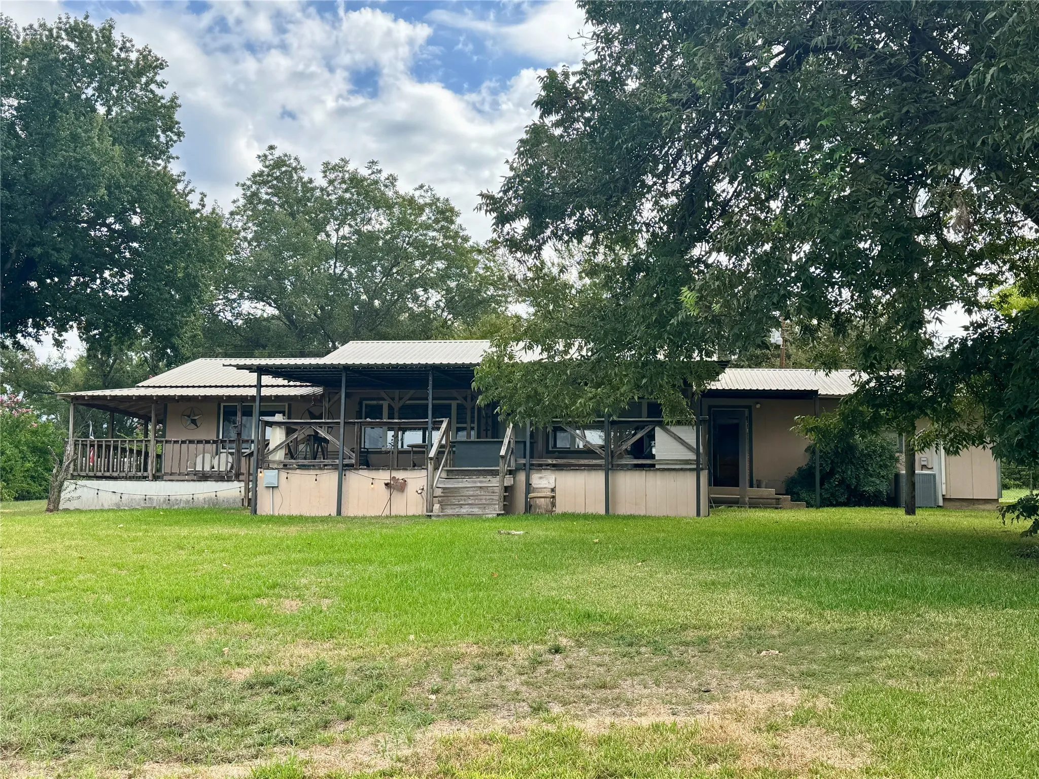 Expansive green lawn with mature trees and a multi-level deck featuring a wood railing