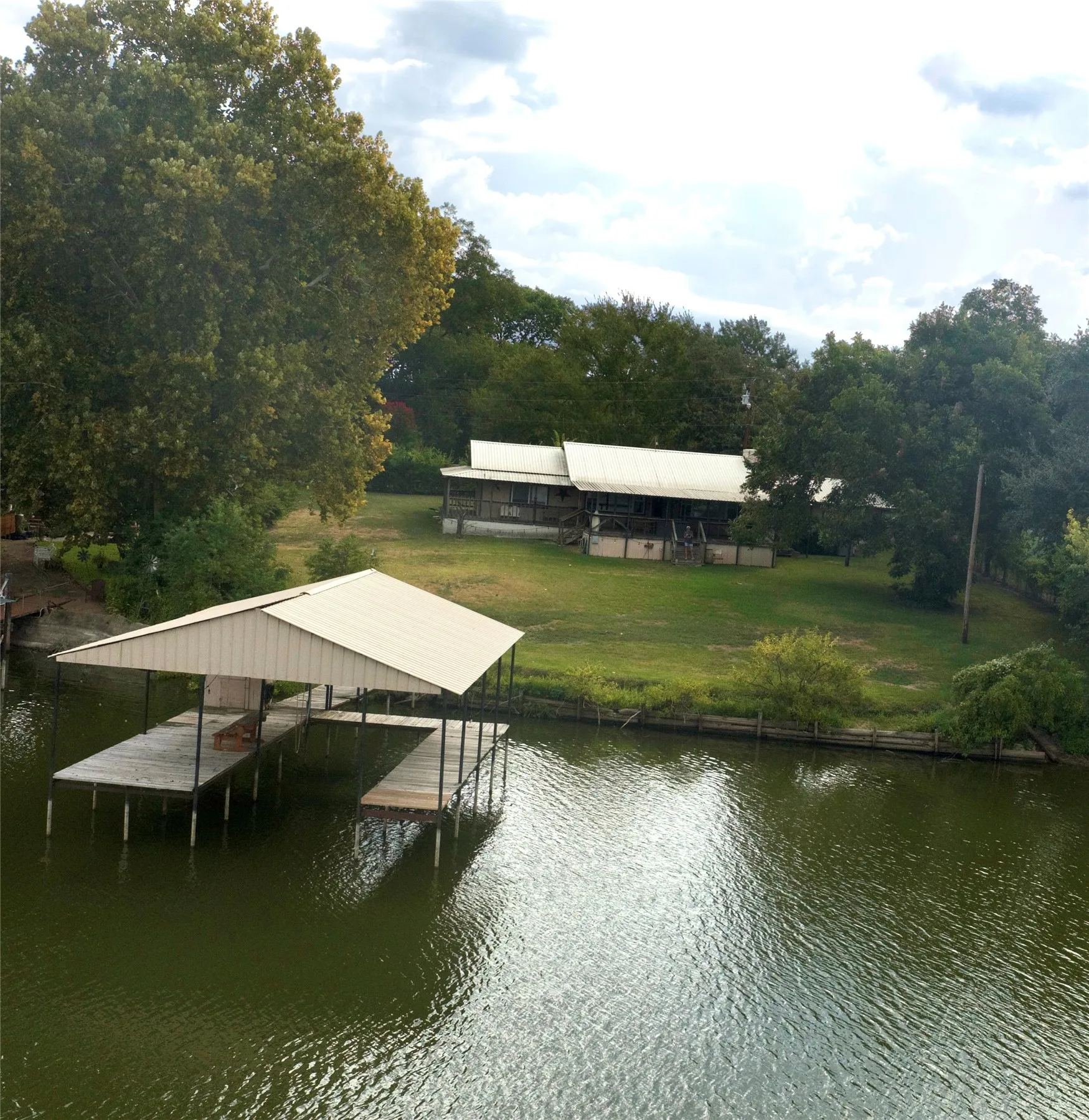 Waterfront property featuring a private boat dock with covered slip, expansive green space, and mature trees