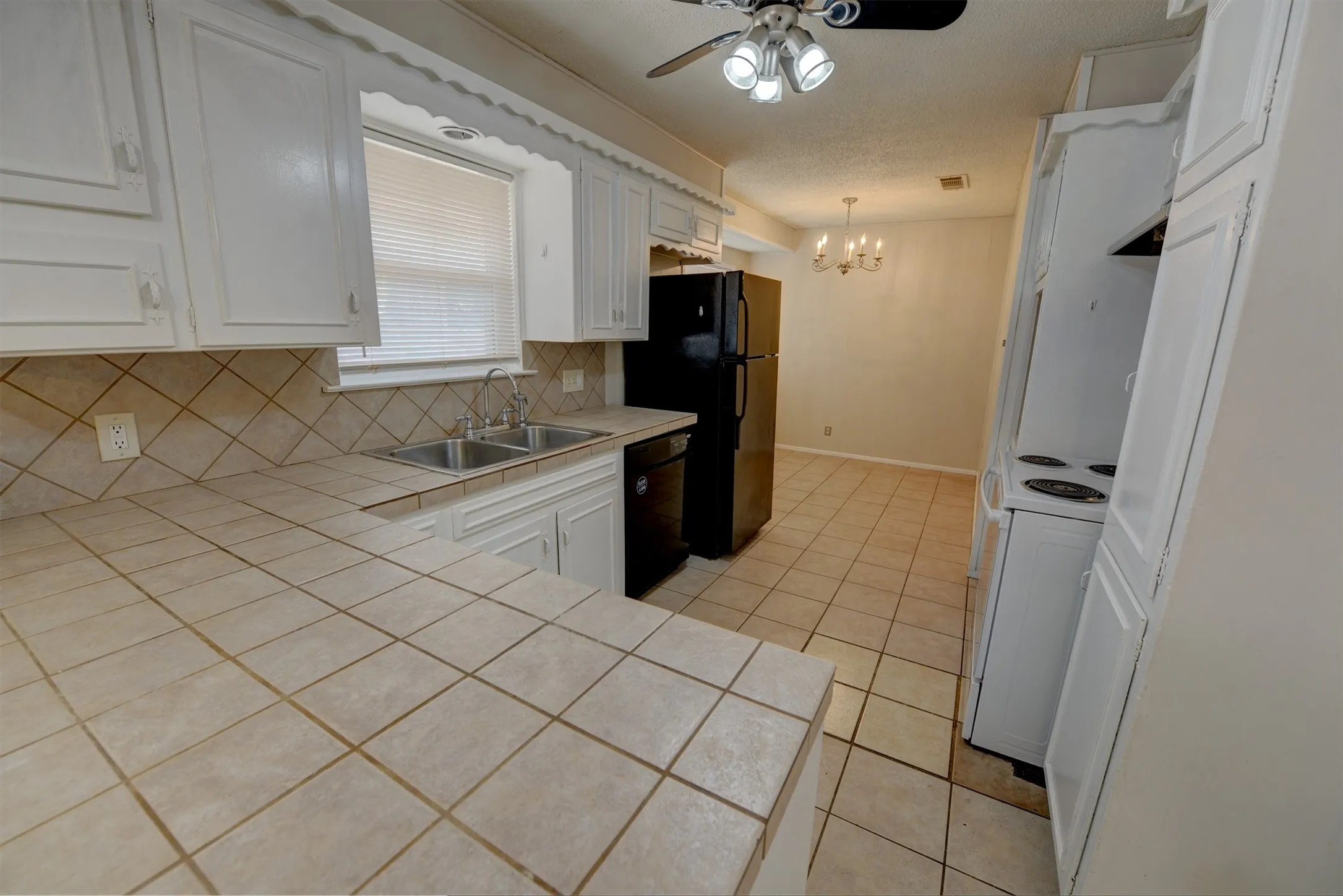 Tile countertops with a diagonal tile backsplash, double basin sink, white cabinetry, and tile flooring