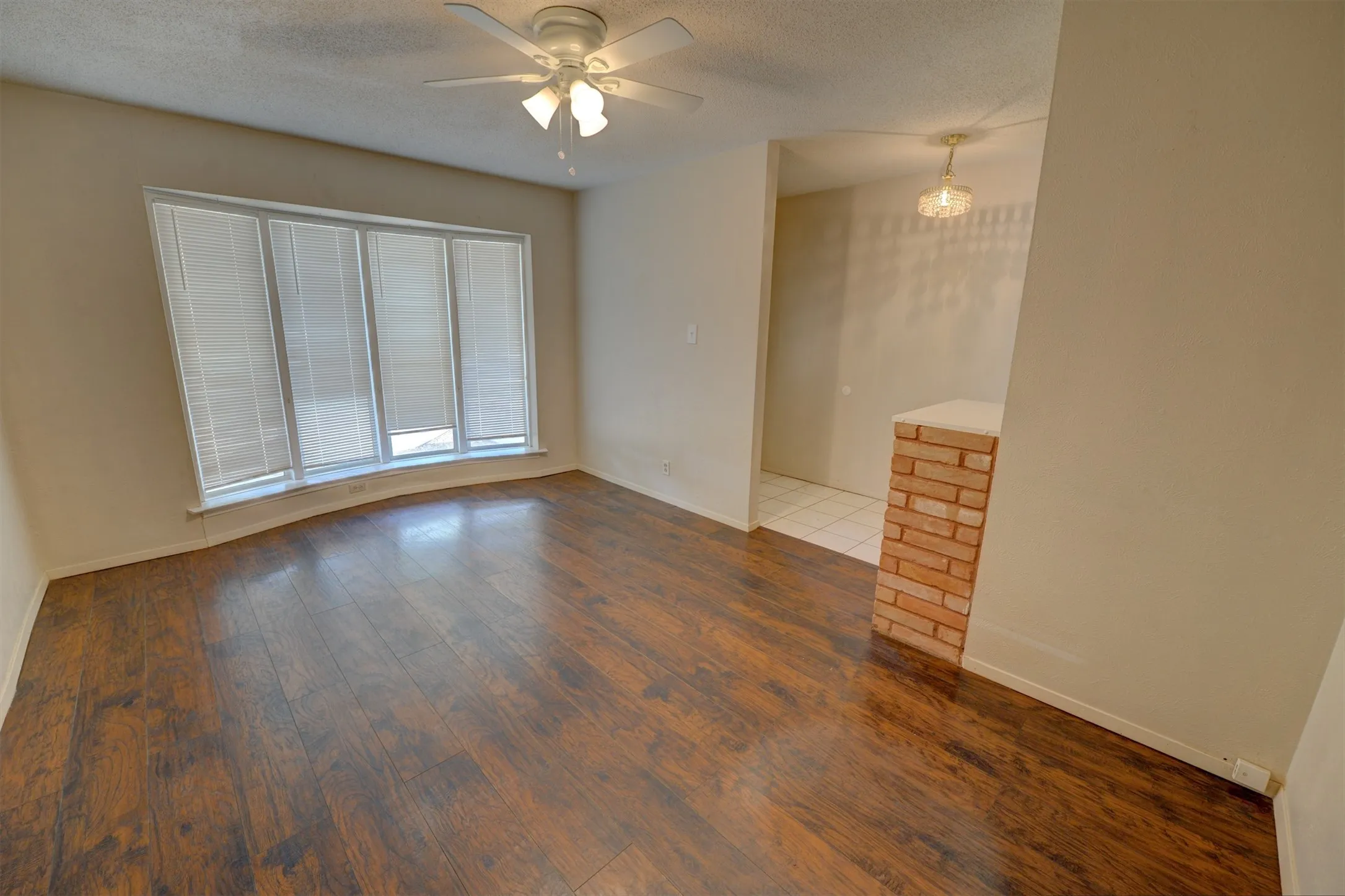 Expansive room featuring wood-finish flooring, a bay window with blinds, and a ceiling fan