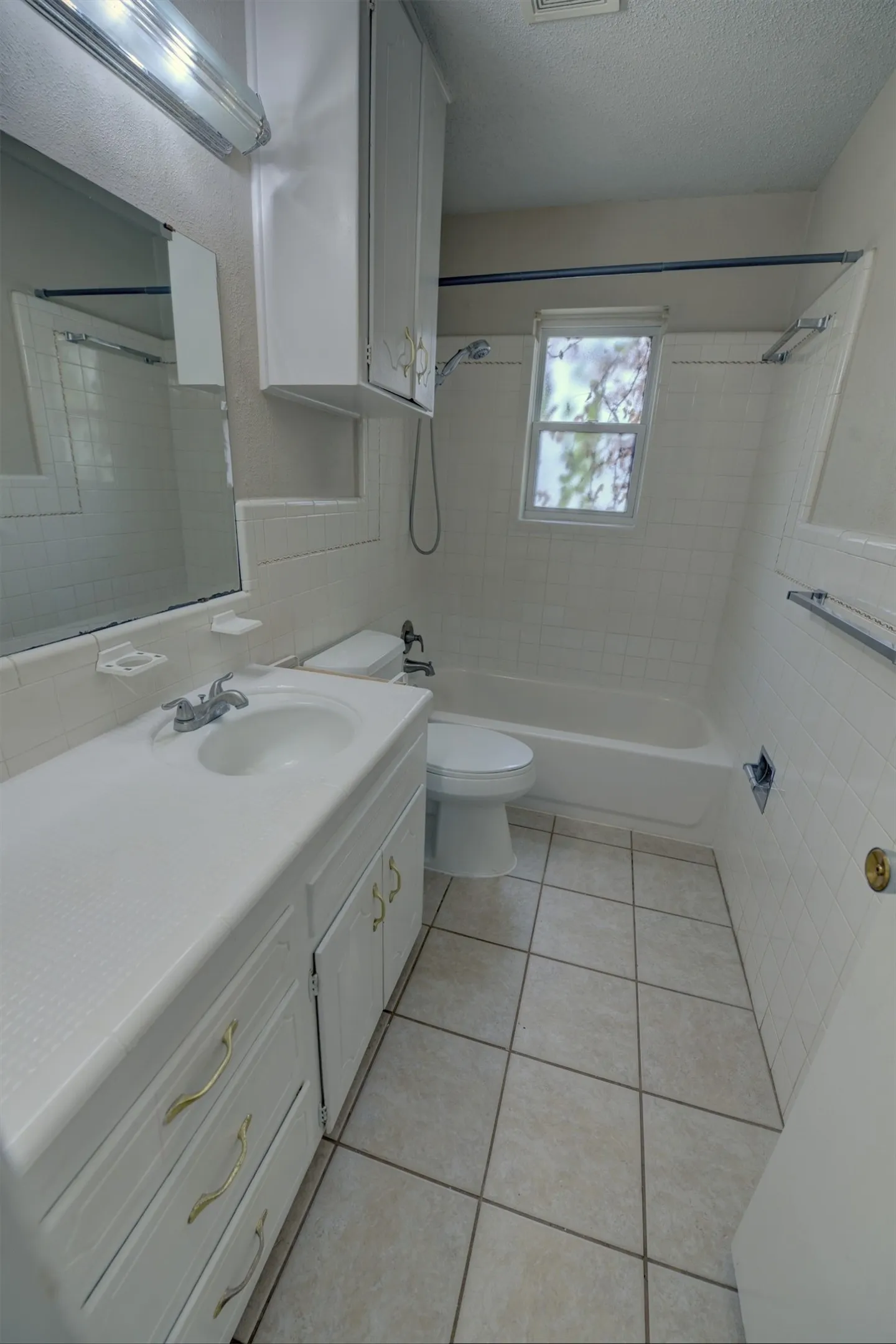 Bathroom featuring a single vanity, built-in cabinetry, ceramic tile flooring, a bathtub with an integrated shower, and a window