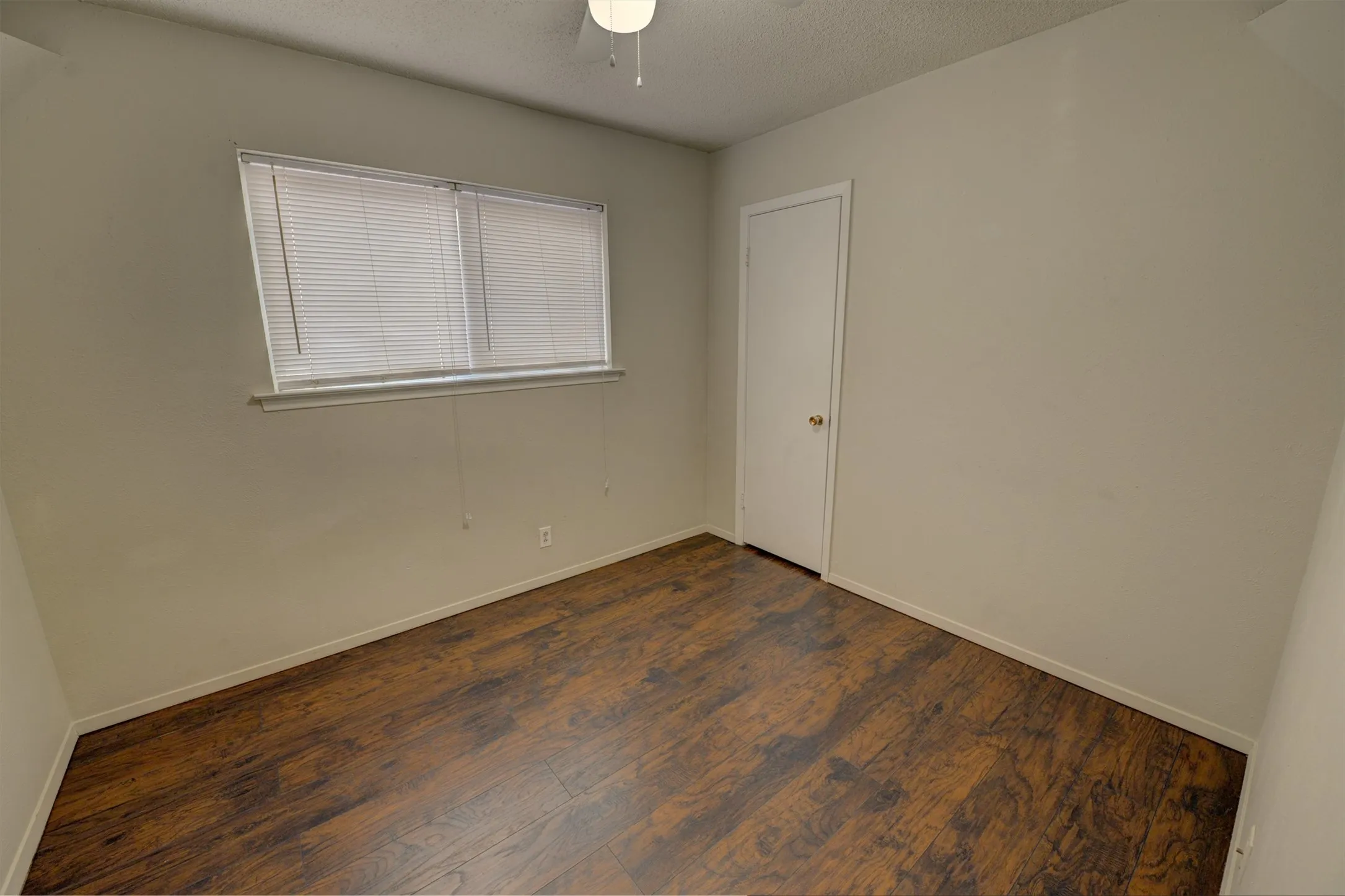 Wood-finish flooring, white walls, ceiling fan, and window with blinds