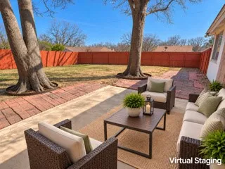 Expansive backyard featuring a red wooden privacy fence, mature trees, a concrete patio, and a brick paver patio area