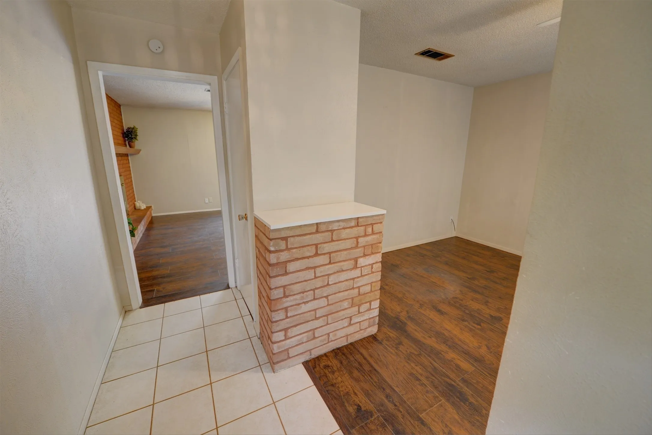 Wood-finish flooring with a brick accent wall and white tile entry