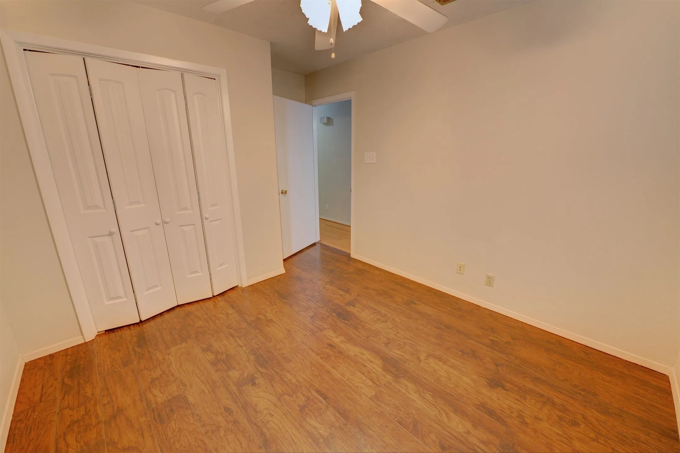 Wood-finish flooring, white bi-fold closet doors, and a ceiling fan with integrated lighting