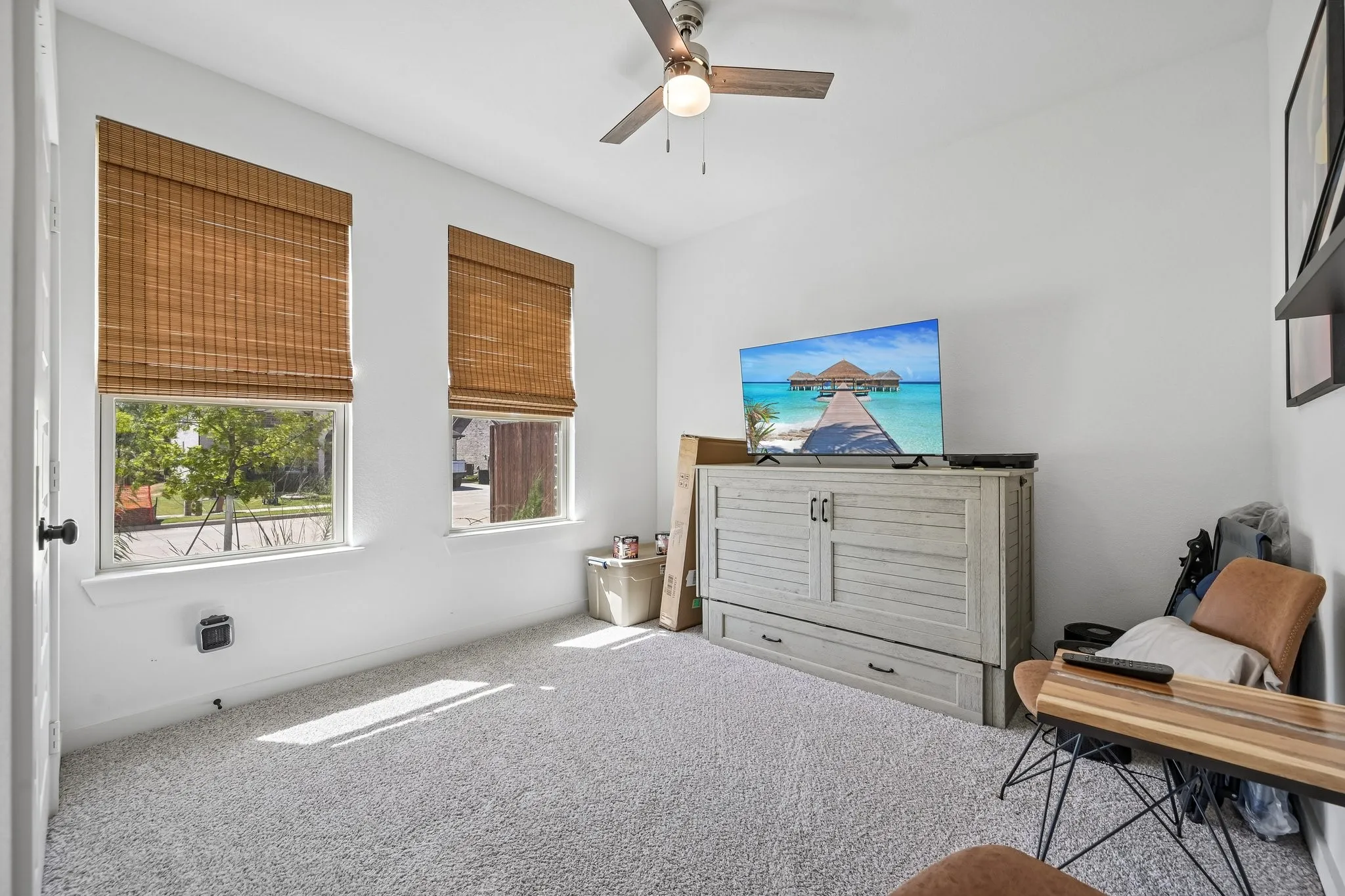 Two windows with woven wood blinds, ceiling fan with light fixture, and light-colored carpet flooring