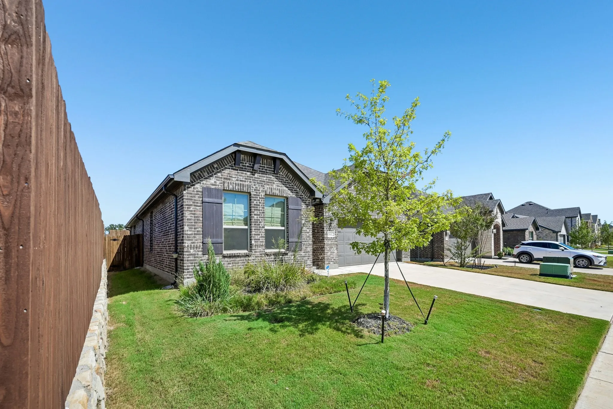 Brick exterior with decorative shutters, front yard landscaping, an established tree, and a concrete driveway
