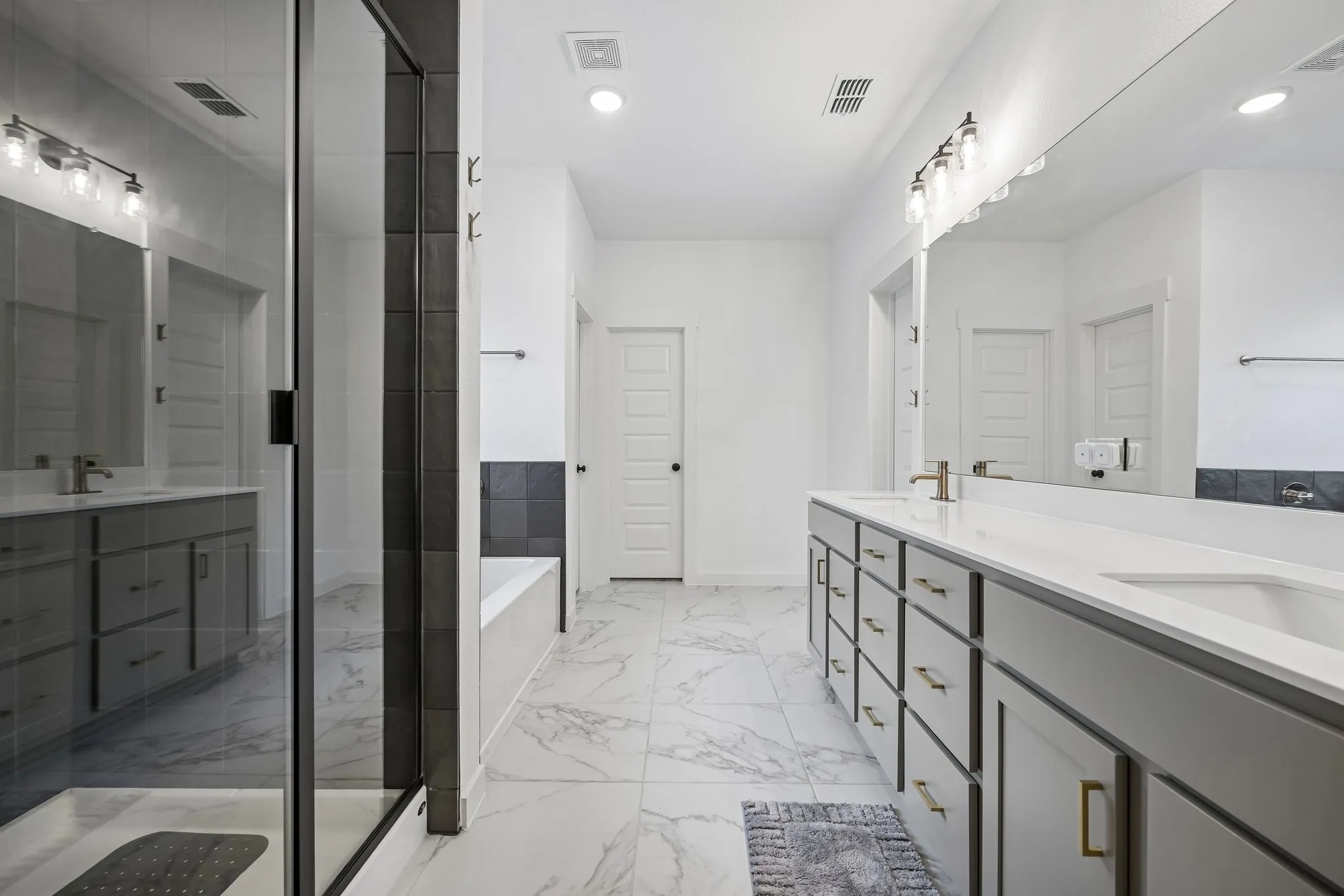 Walk-in shower with glass enclosure, dual vanity with undermount sinks, white countertops, and expansive wall mirror