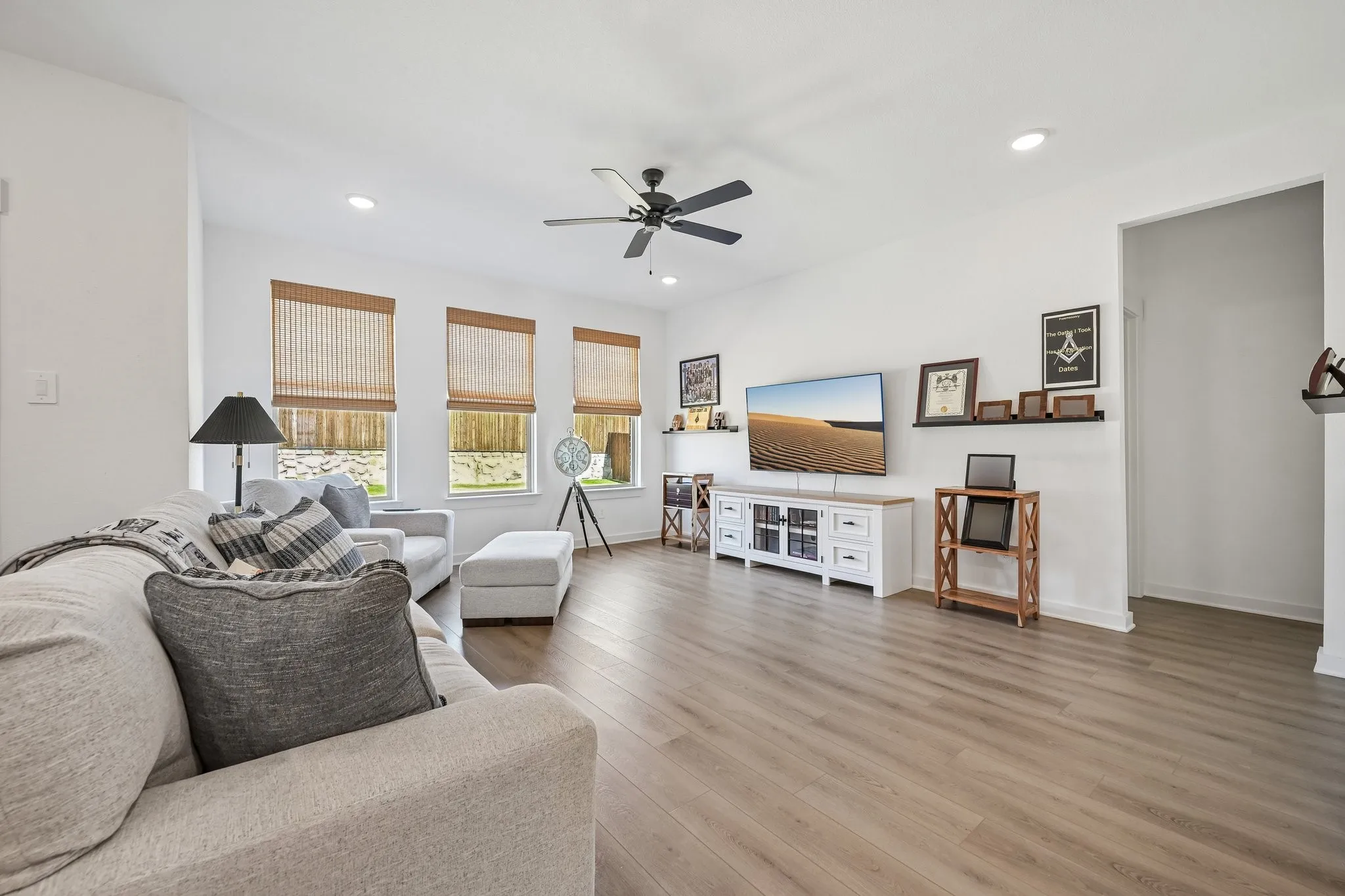 Wood-finish flooring, recessed lighting, ceiling fan, multiple windows with blinds, and white wall finishes