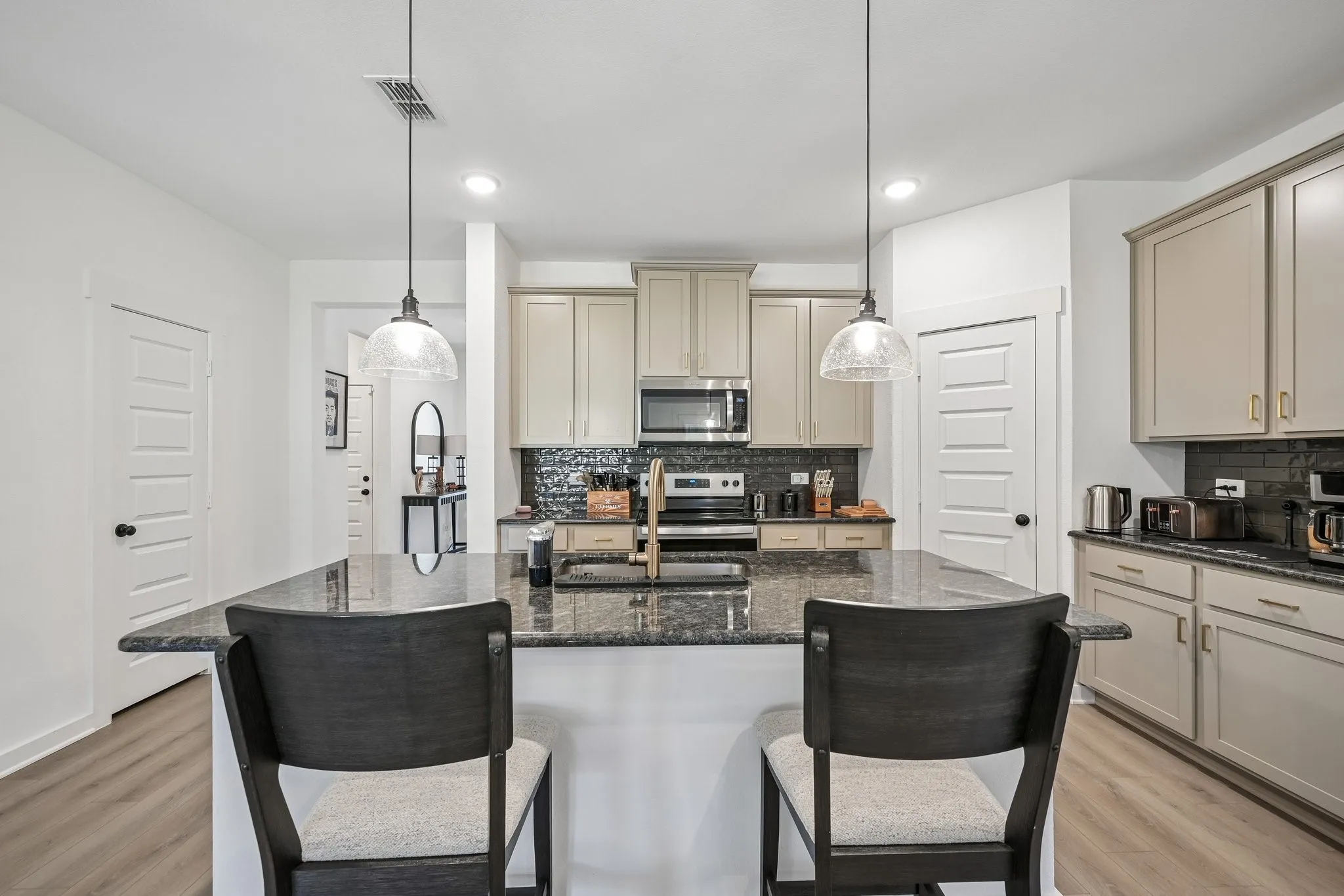 Kitchen featuring an expansive island with a dark countertop, pendant lighting, built-in microwave, and wood-finish flooring