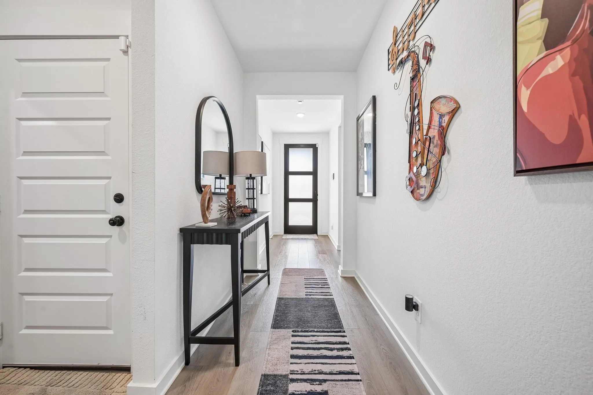 Hallway featuring wood-finish flooring, white walls, and a modern paneled door