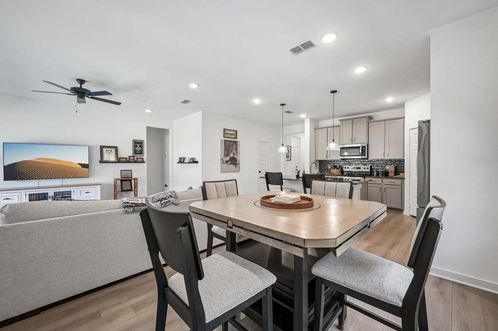 Open-concept living space featuring wood-finish flooring, recessed lighting, a ceiling fan, and a kitchen with stainless steel appliances and a tile backsplash