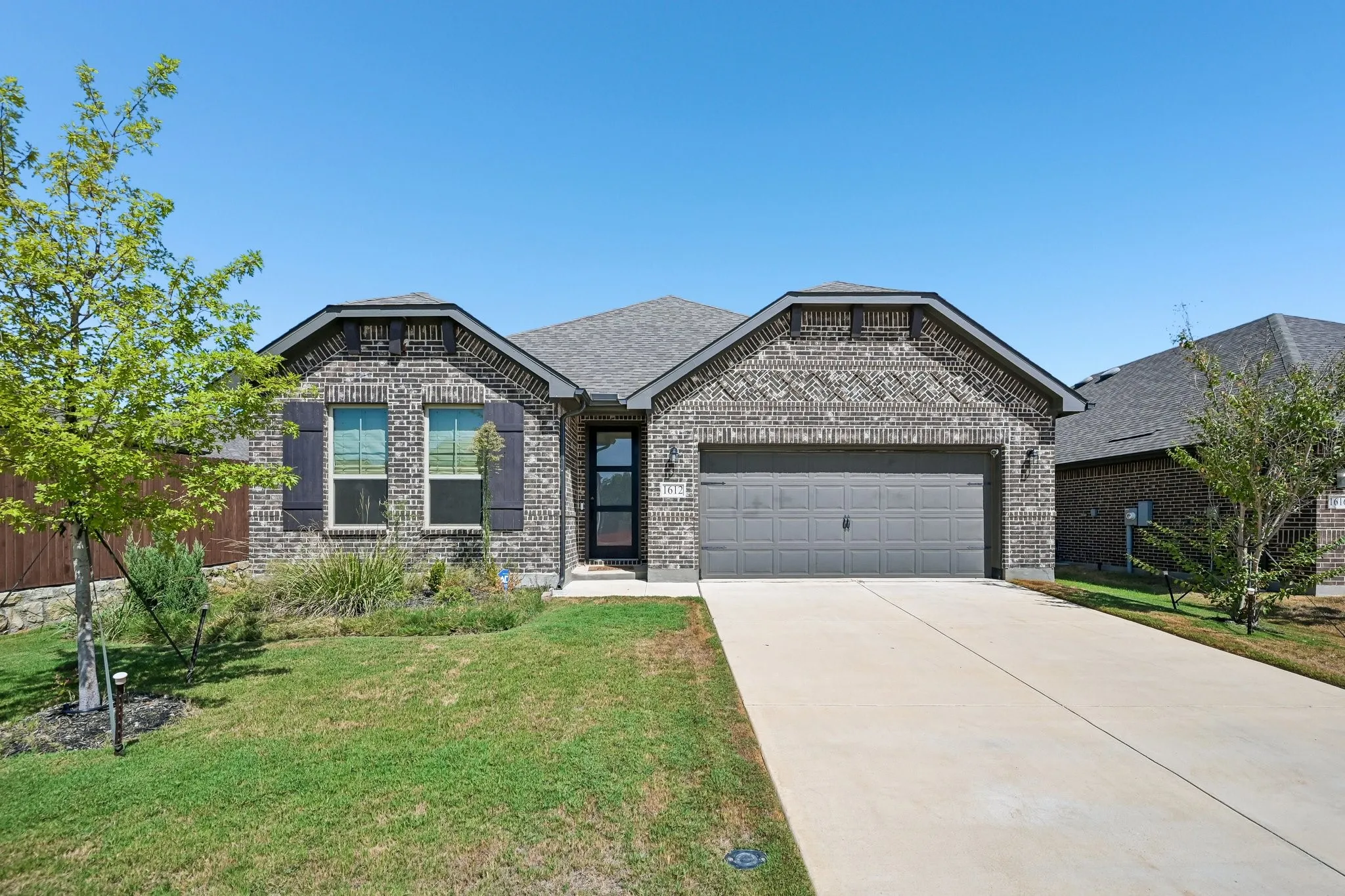 Brick exterior with decorative detailing, attached two-car garage, concrete driveway, front landscaping, and a covered entry