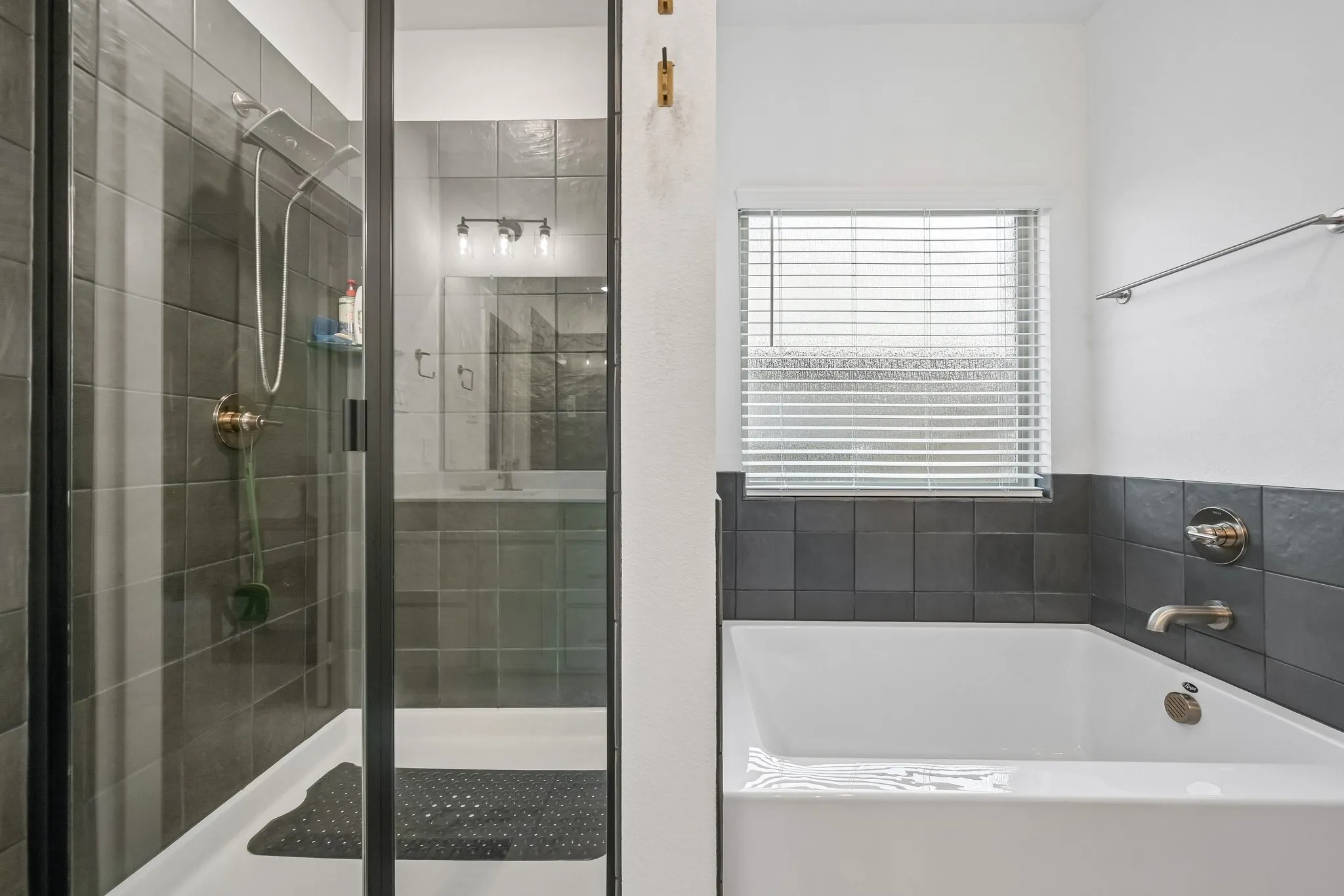 Frameless glass shower enclosure with dark tile surround, integrated showerhead, and separate soaking tub with chrome fixtures