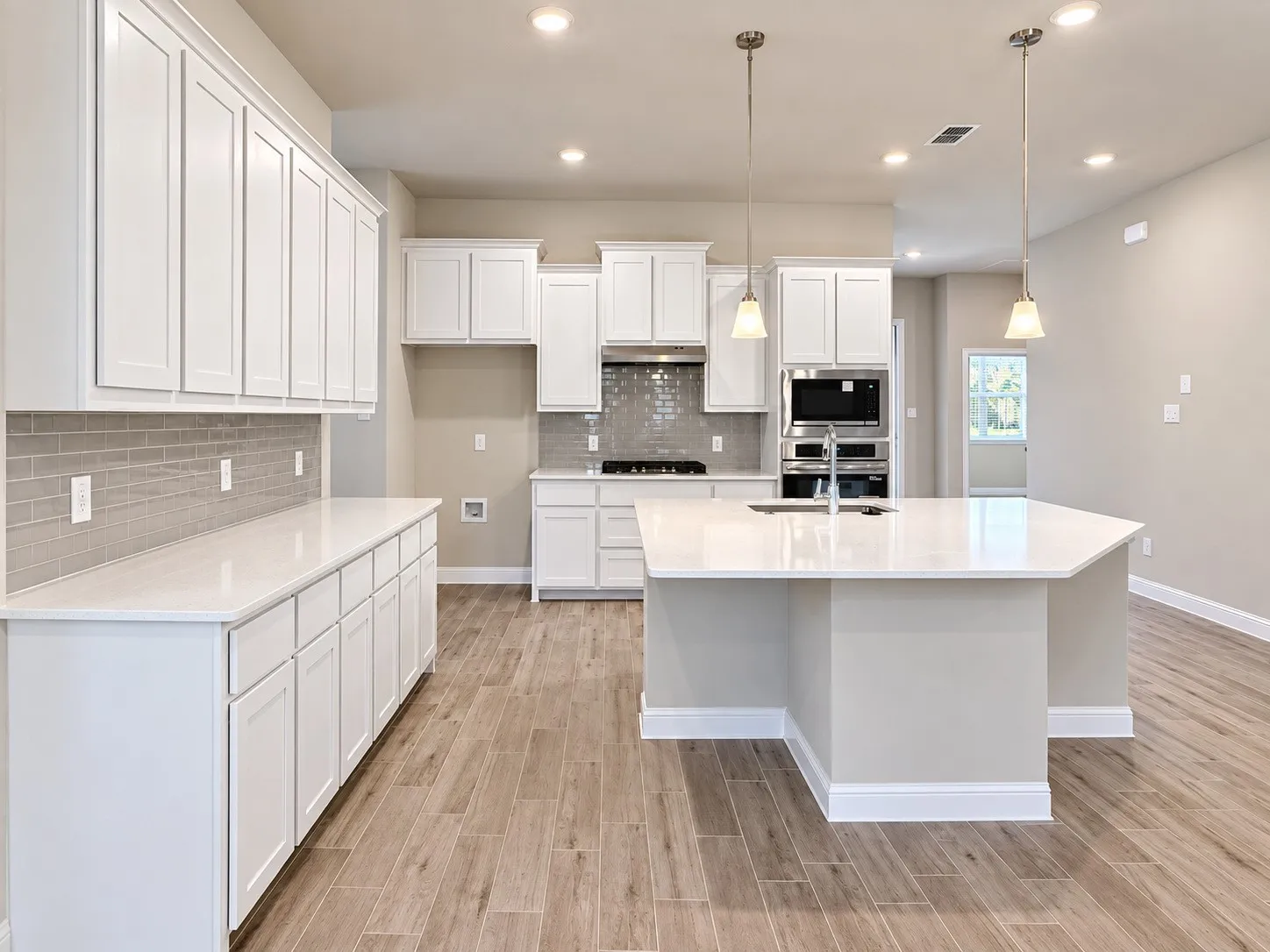 Modern kitchen featuring wood-finish flooring, white cabinetry, a large kitchen island with pendant lighting, integrated stainless steel appliances, and a subway tile backsplash