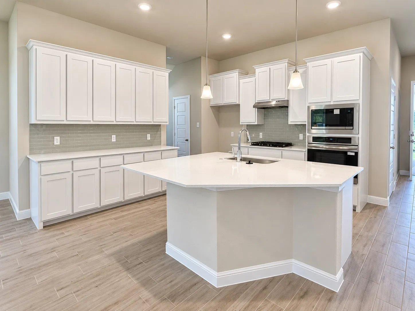 Kitchen featuring an expansive center island, integrated stainless steel appliances, a tiled backsplash, wood-finish flooring, and extensive white cabinetry