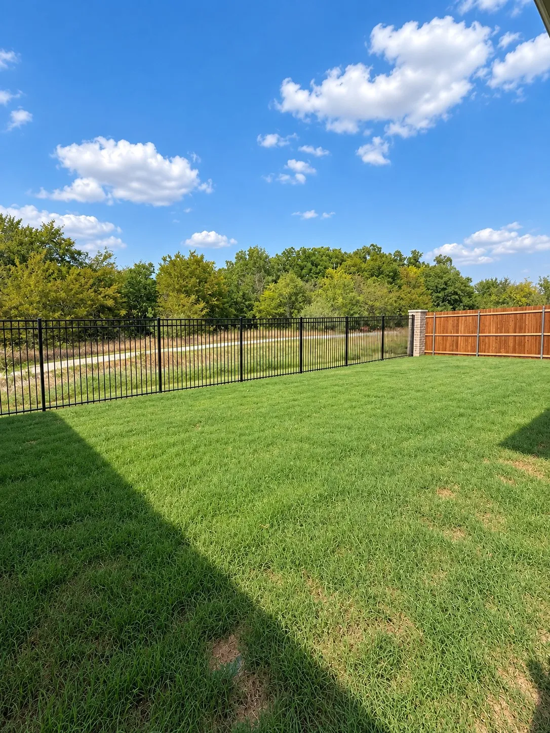 Expansive grassy yard with a black wrought iron fence and a wood privacy fence