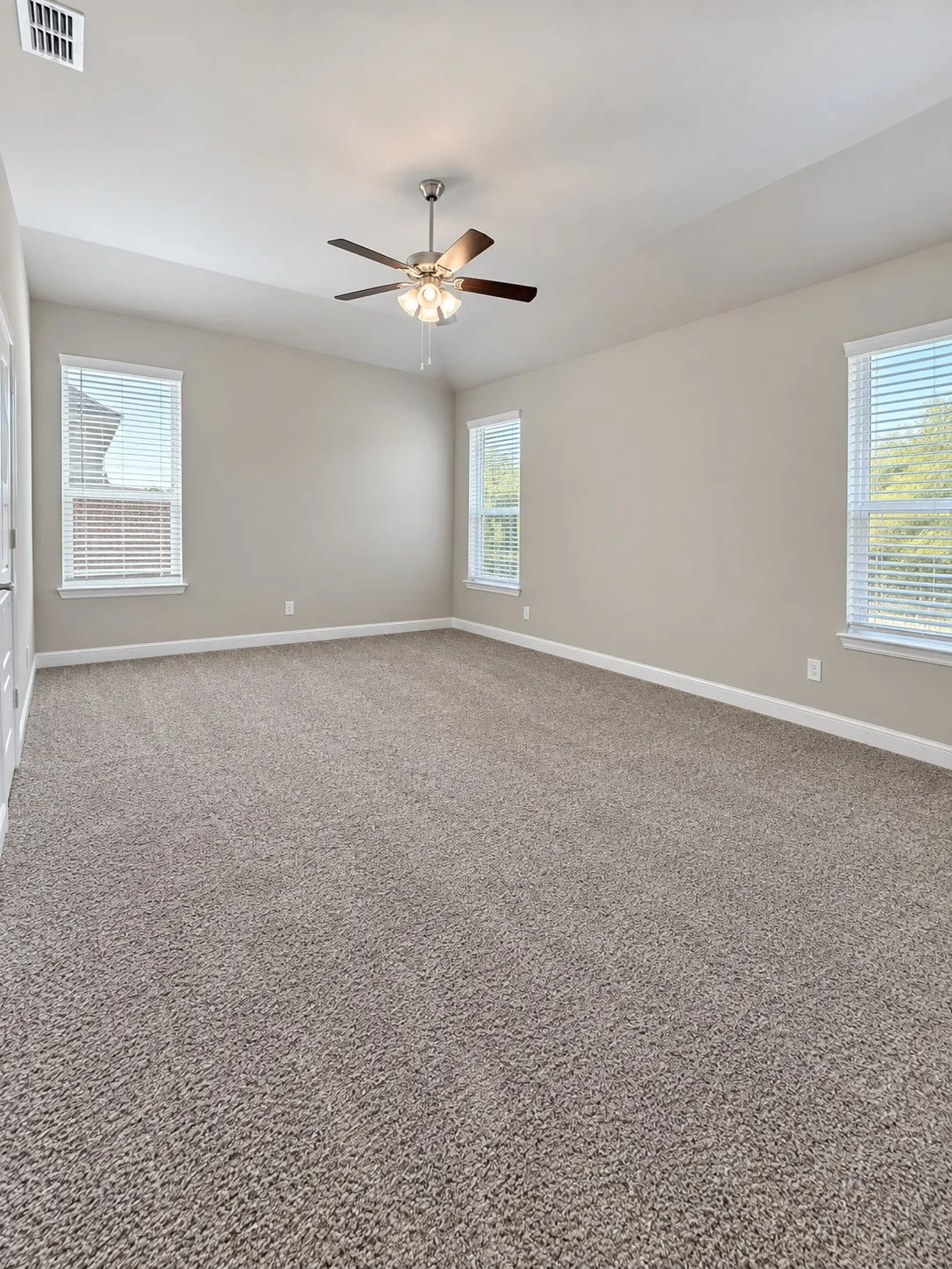 Expansive room featuring neutral-toned carpeting, light-colored walls, multiple windows with blinds, a ceiling fan, and a vaulted ceiling