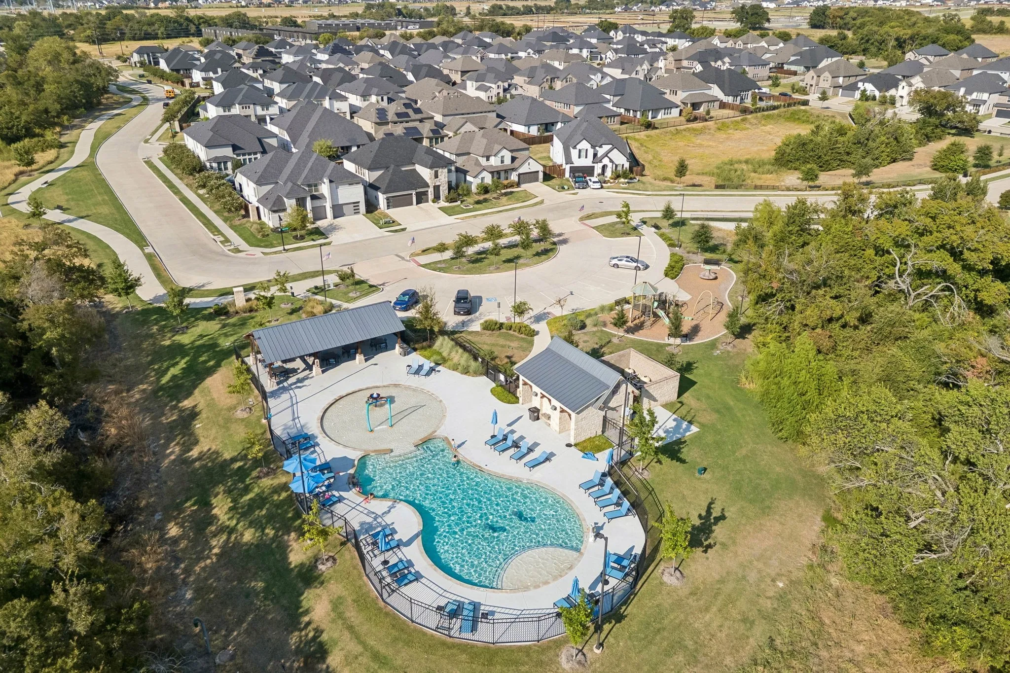 Community pool with integrated splash pad, adjacent covered pavilion, and surrounding lounge areas