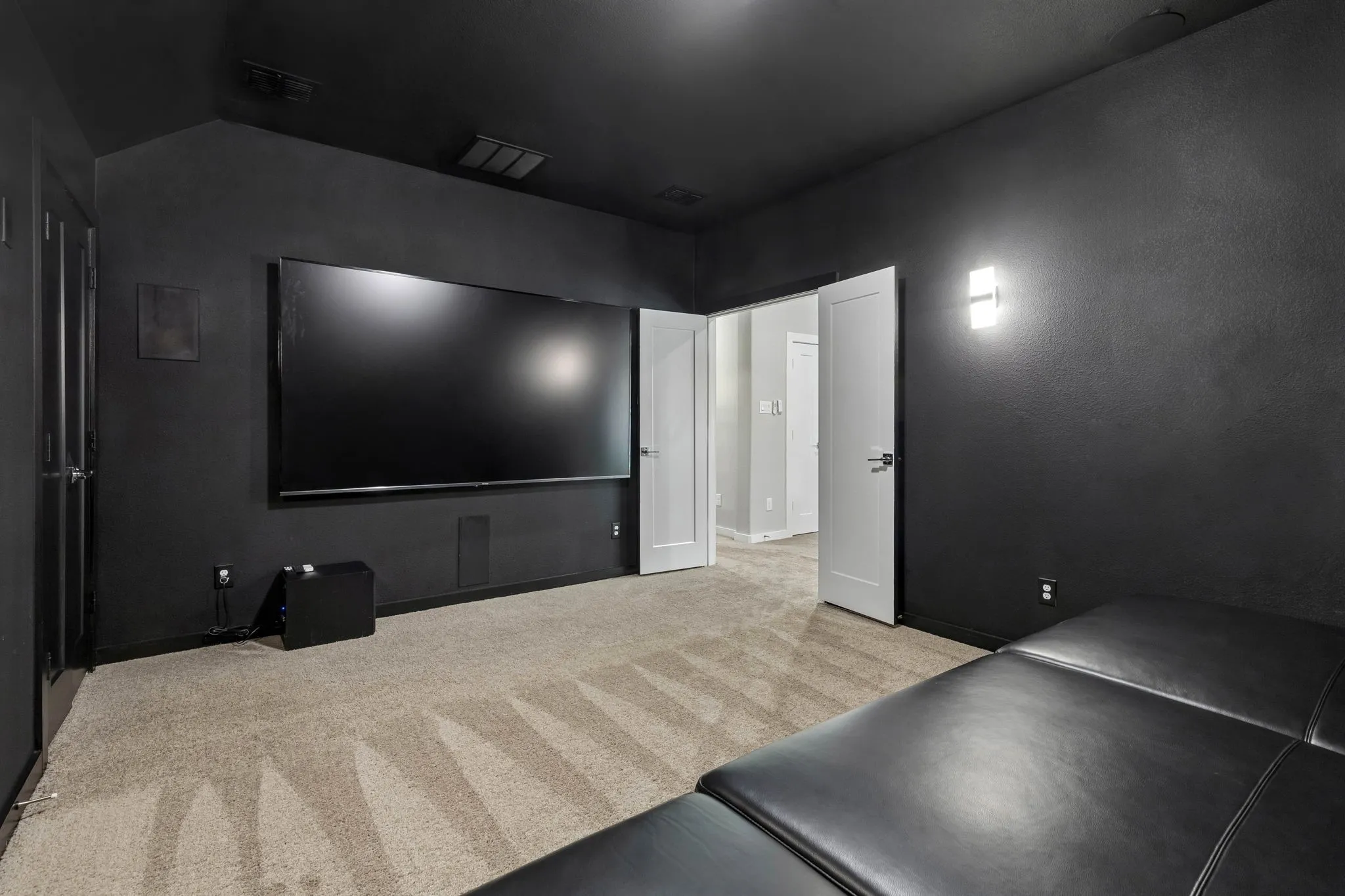 Dedicated media room featuring dark walls and ceiling, wall-mounted display, recessed speaker, and wall sconce lighting