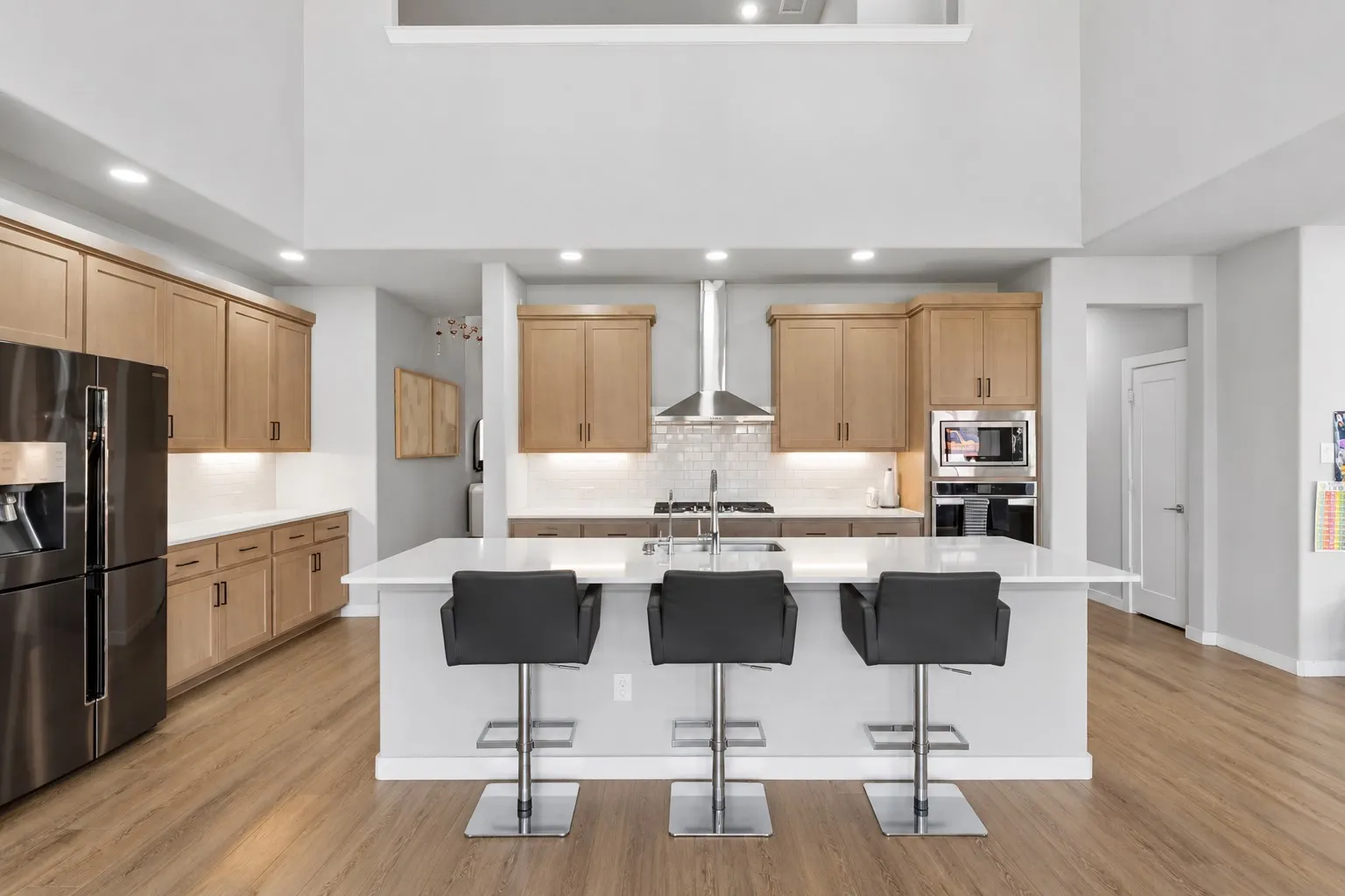 Open-concept kitchen featuring light wood cabinetry, a large kitchen island with counter seating, stainless steel appliances, and wood-finish flooring