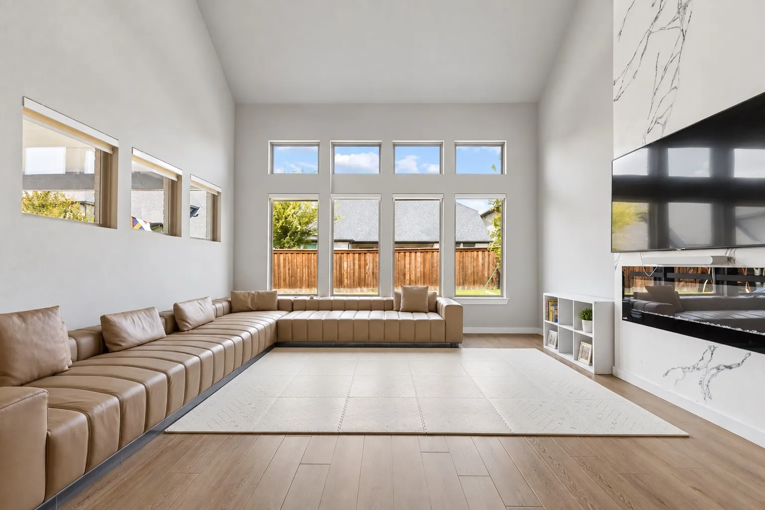 Vaulted ceilings, wood-finish flooring, multiple large windows, and a built-in entertainment wall with a linear fireplace
