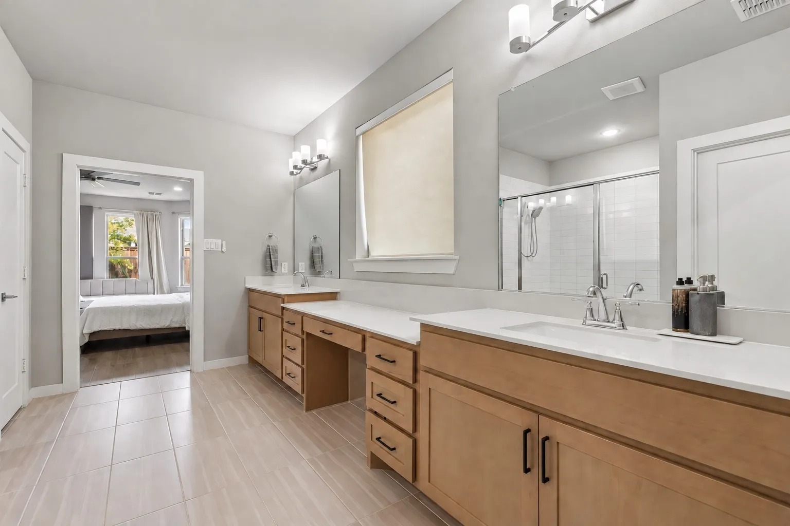 Dual wood-finish vanities with light countertops, separate shower enclosure with glass doors, rectangular mirrors, and light tile flooring