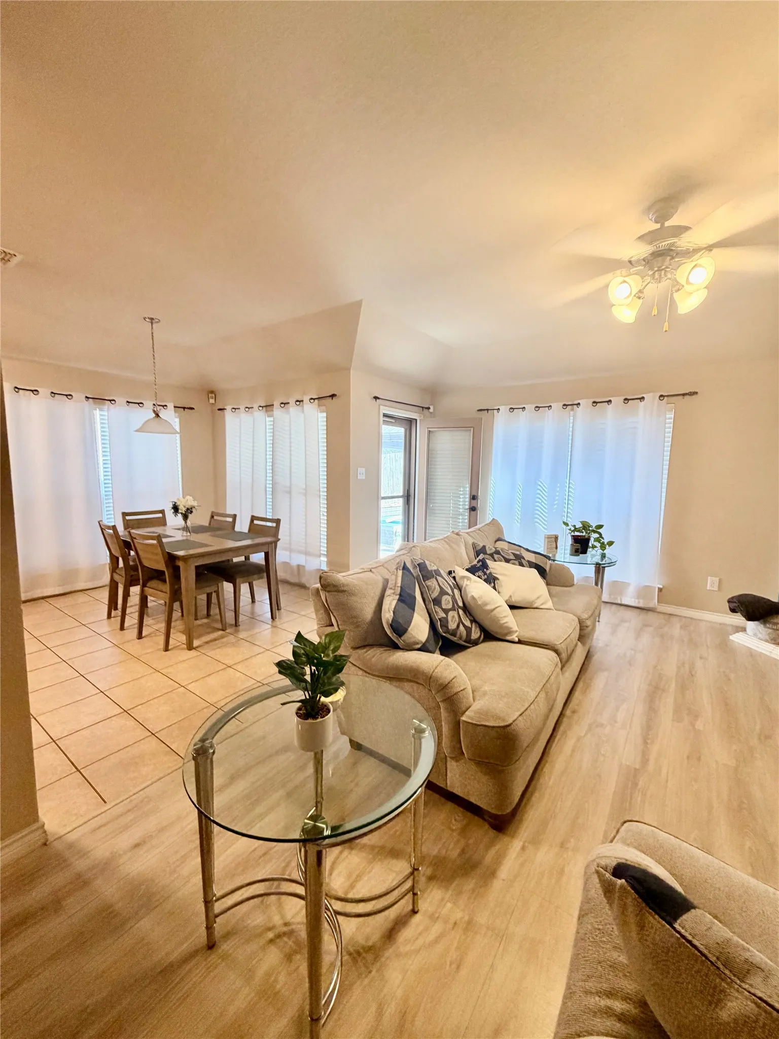 Wood-finish flooring, tiled dining area, ceiling fan with integrated lighting, multiple windows with blinds, and pendant lighting fixture