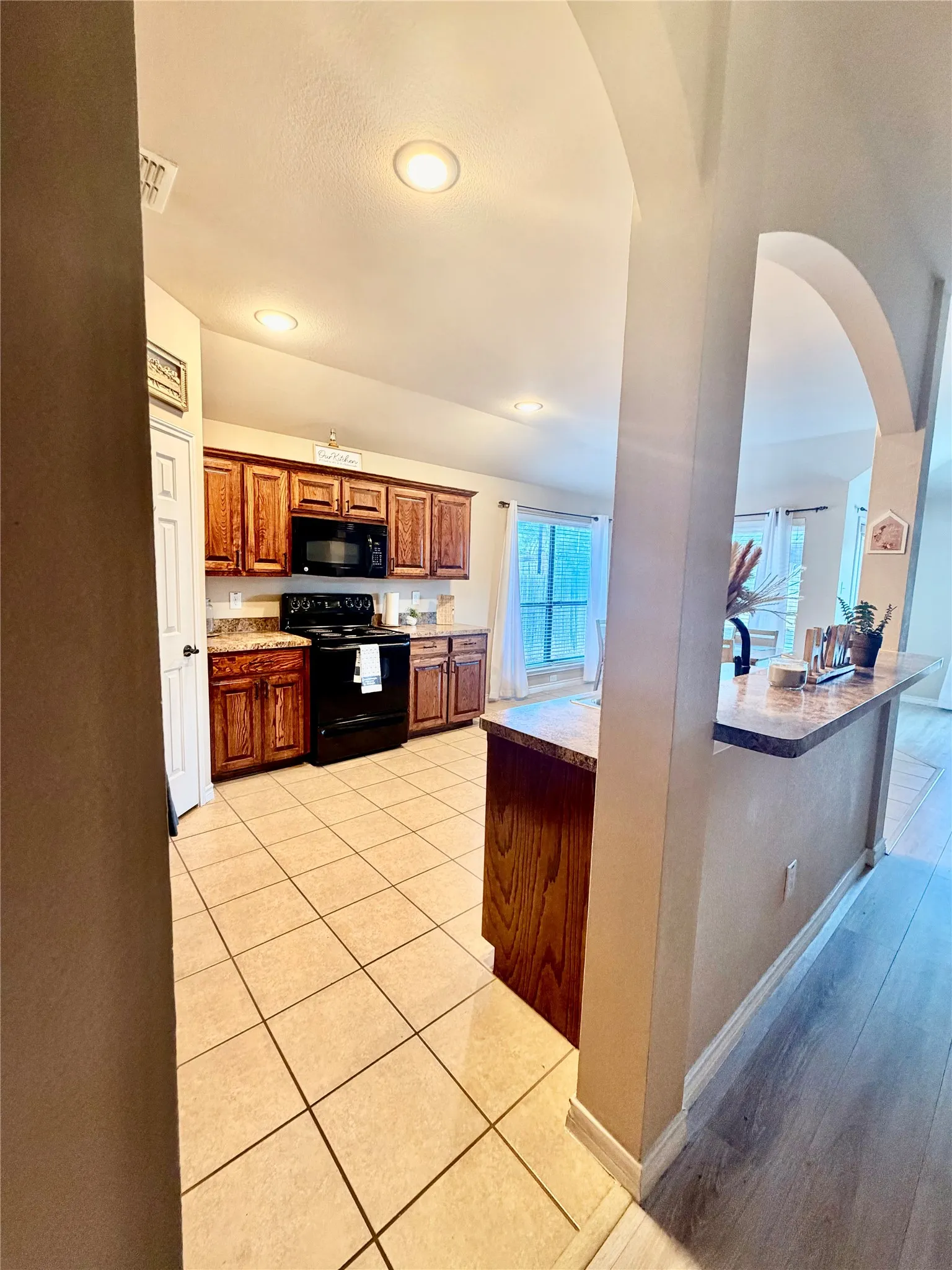 Kitchen featuring wood cabinetry, tile flooring, recessed lighting, and black appliances