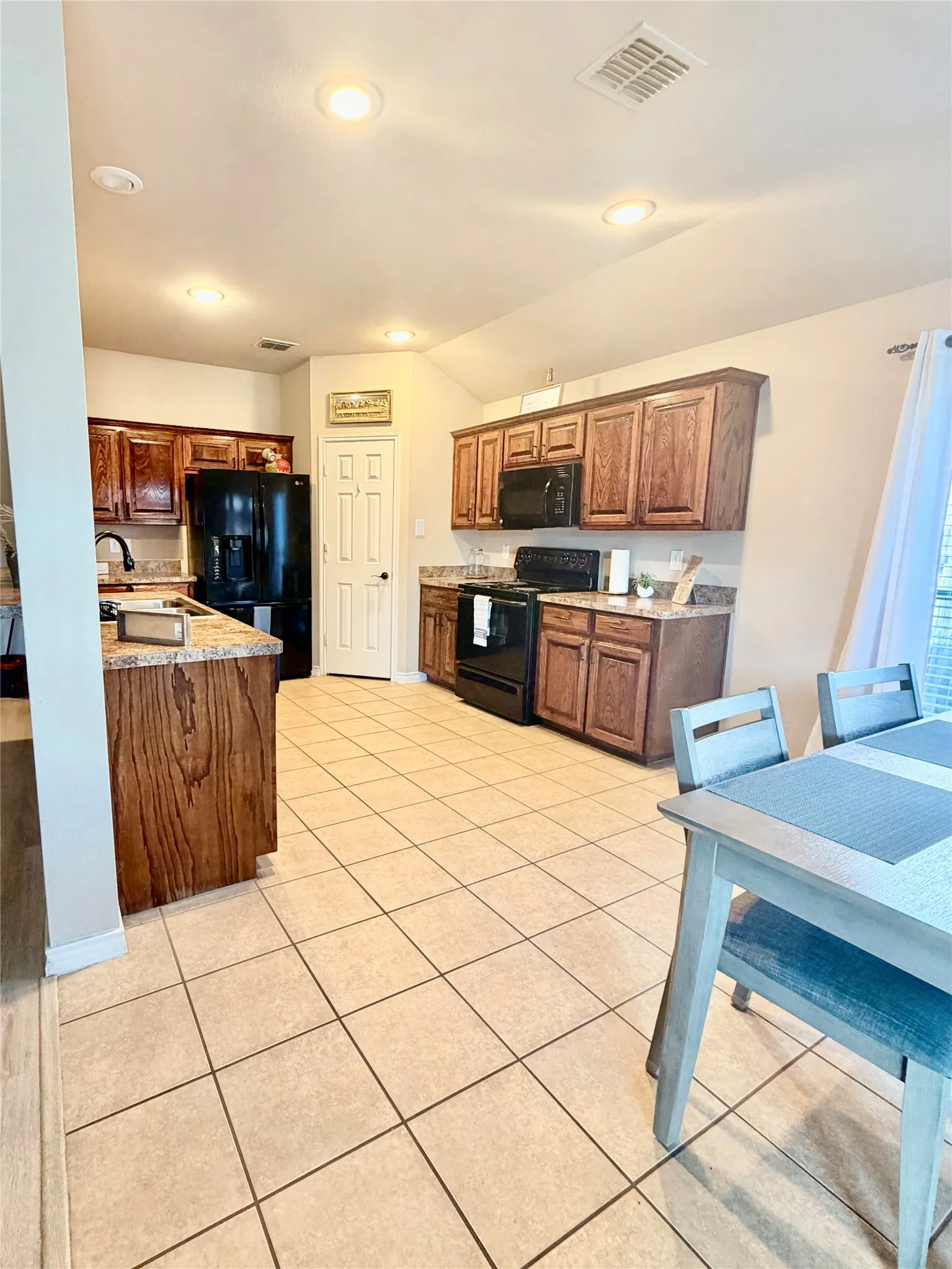 Kitchen featuring wood cabinetry, dark countertops, black appliances, recessed lighting, and tile flooring