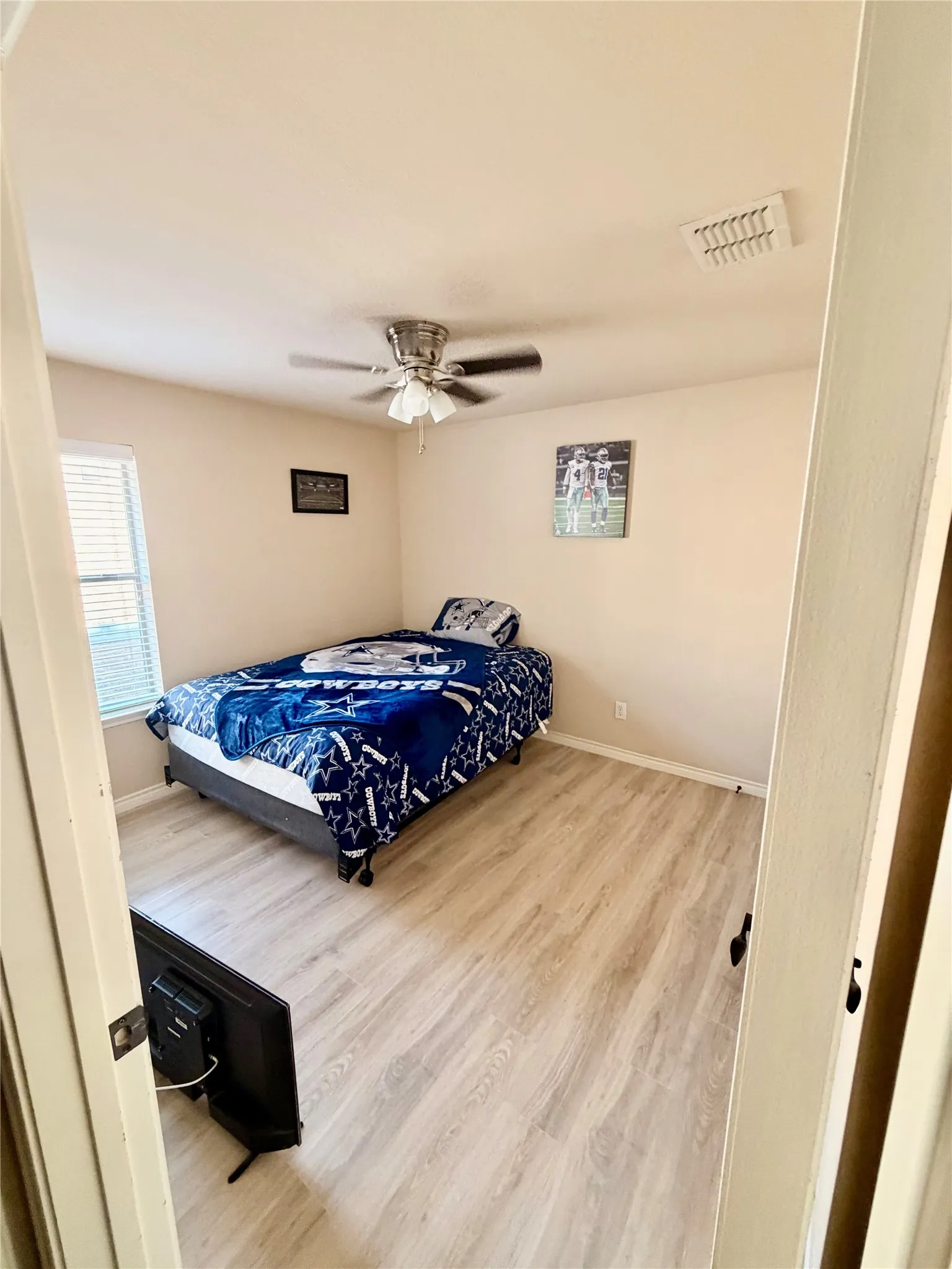 Wood-finish flooring, ceiling fan with integrated lighting, and a single window with blinds