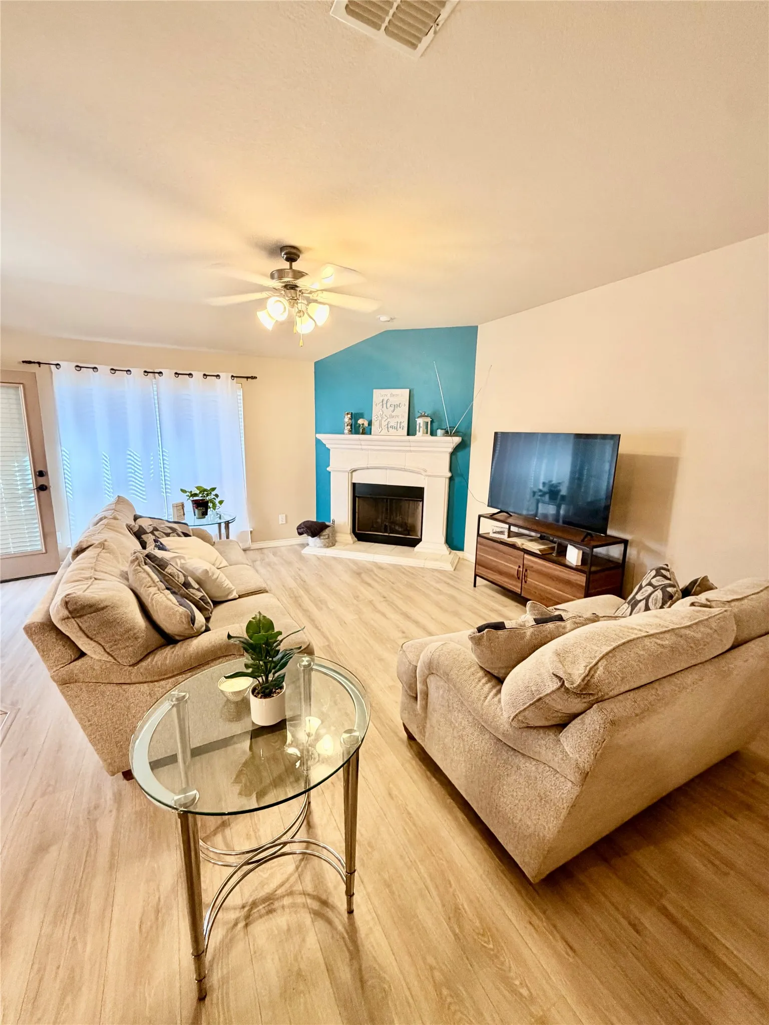 Spacious living area featuring wood-finish flooring, a ceiling fan, and a fireplace with a decorative mantel