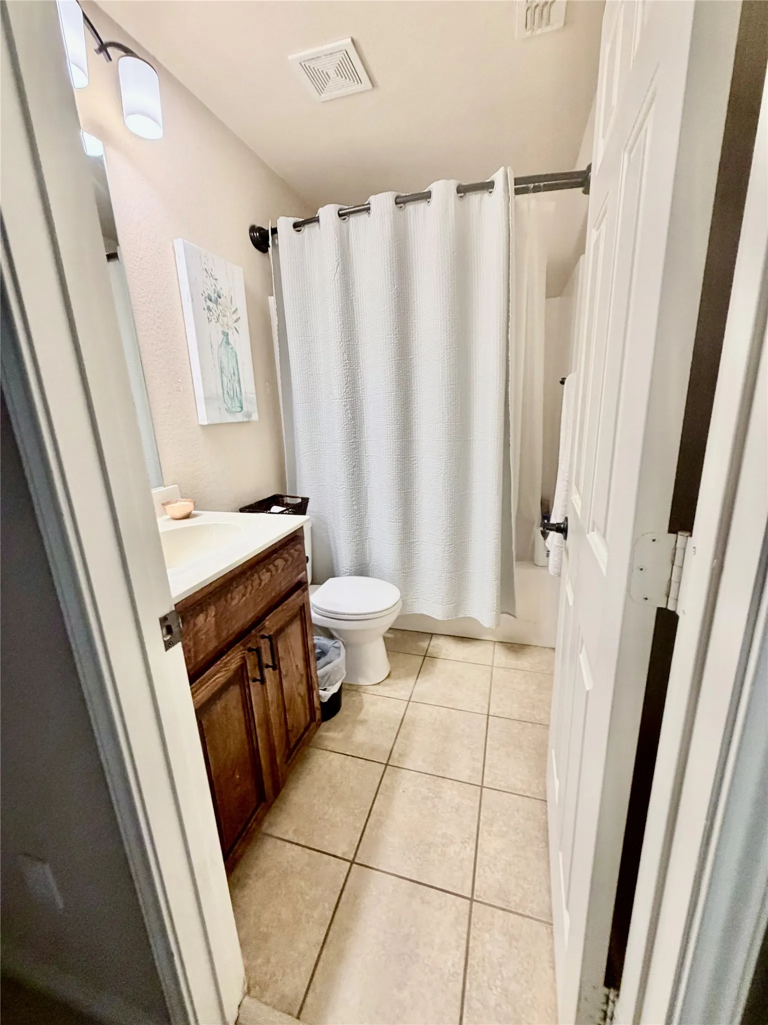 Full bathroom featuring a wood-finish vanity with an integrated sink, ceramic tile flooring, and a shower-tub combination