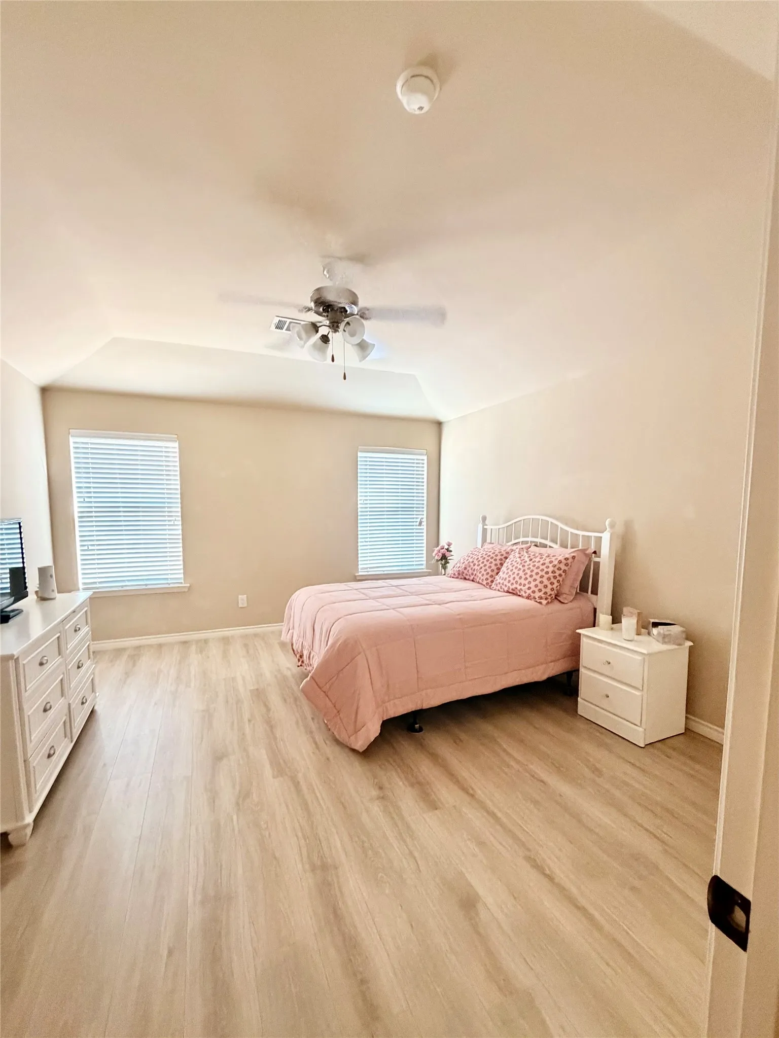 Vaulted ceiling with a ceiling fan, two windows with blinds, and wood-finish flooring