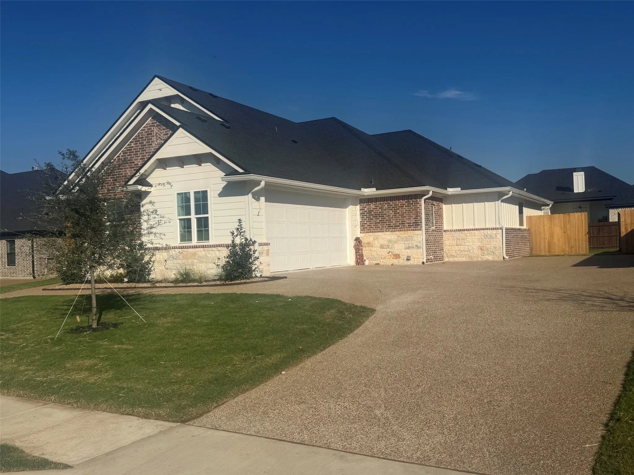 Exterior featuring a dark shingle roof, mixed material facade with brick and stone accents, light-colored siding, an attached garage, and a concrete driveway