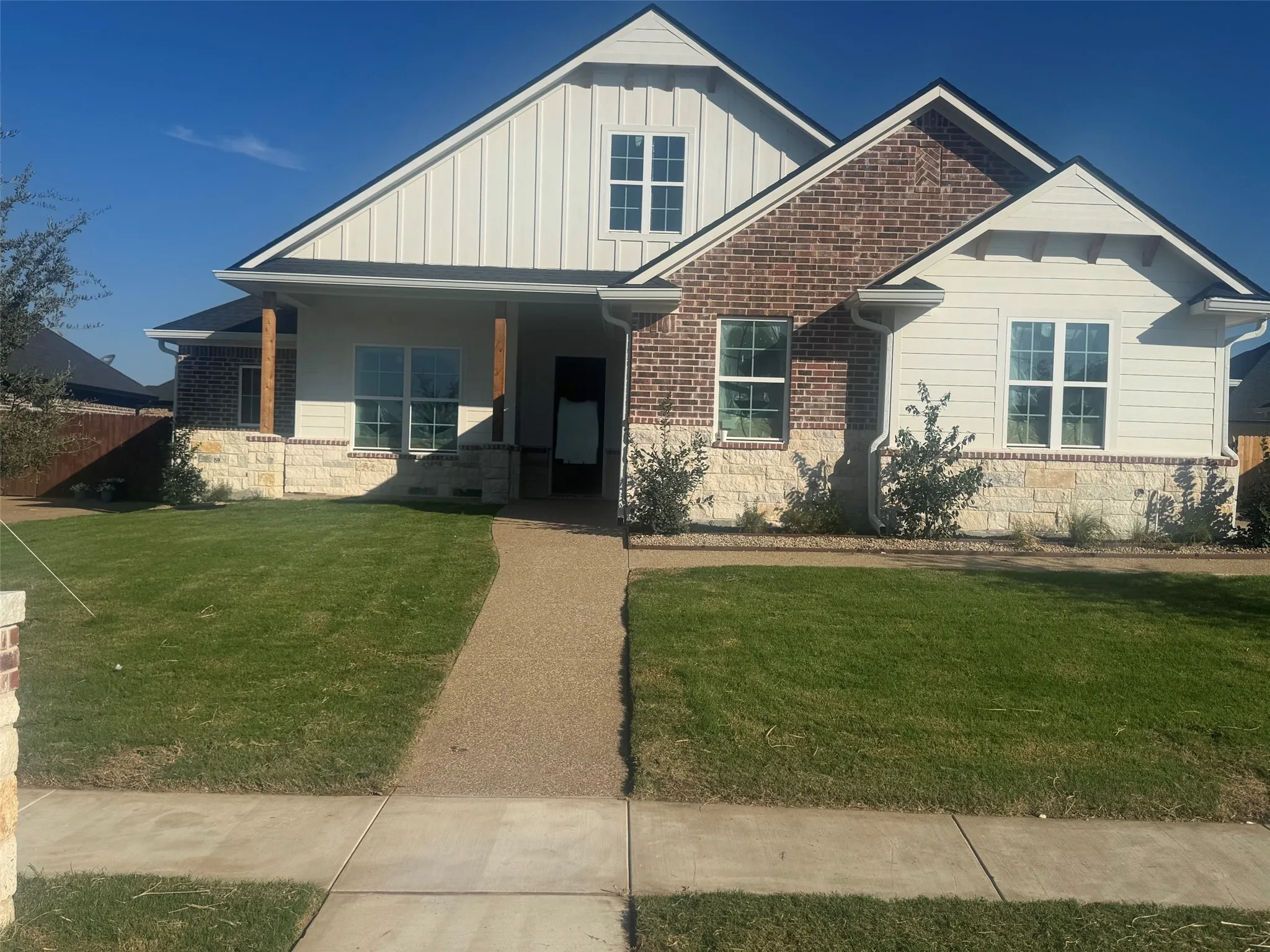 Exterior featuring a blend of brick and stone, vertical siding accents, a covered entry, and a gravel pathway