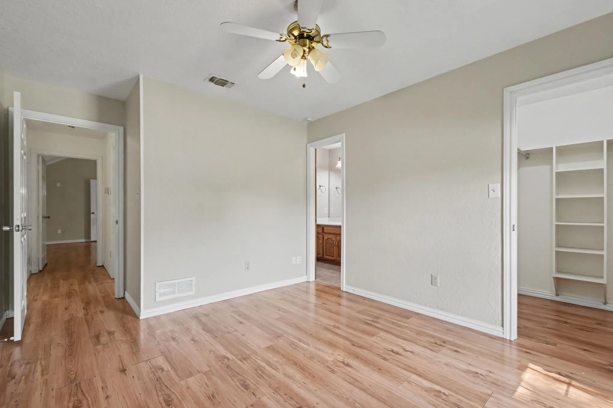Expansive room with wood-finish flooring, a ceiling fan, and a built-in closet system