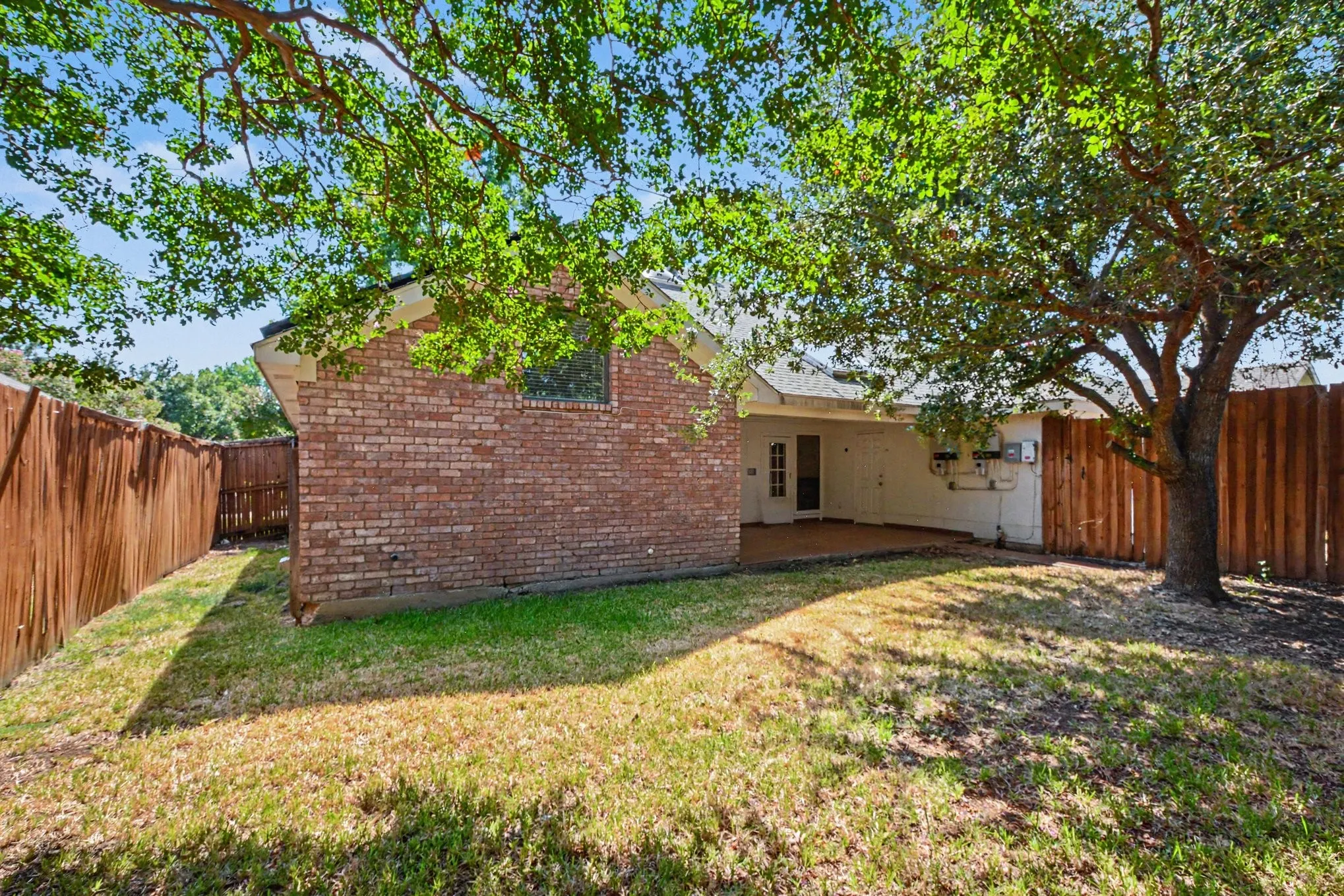 Expansive backyard space featuring mature trees, a covered patio, and a brick exterior