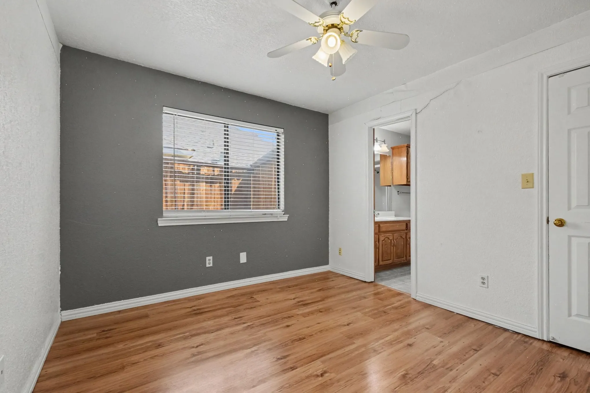 Wood-finish flooring, ceiling fan with integrated lighting, window with blinds, and a white paneled door