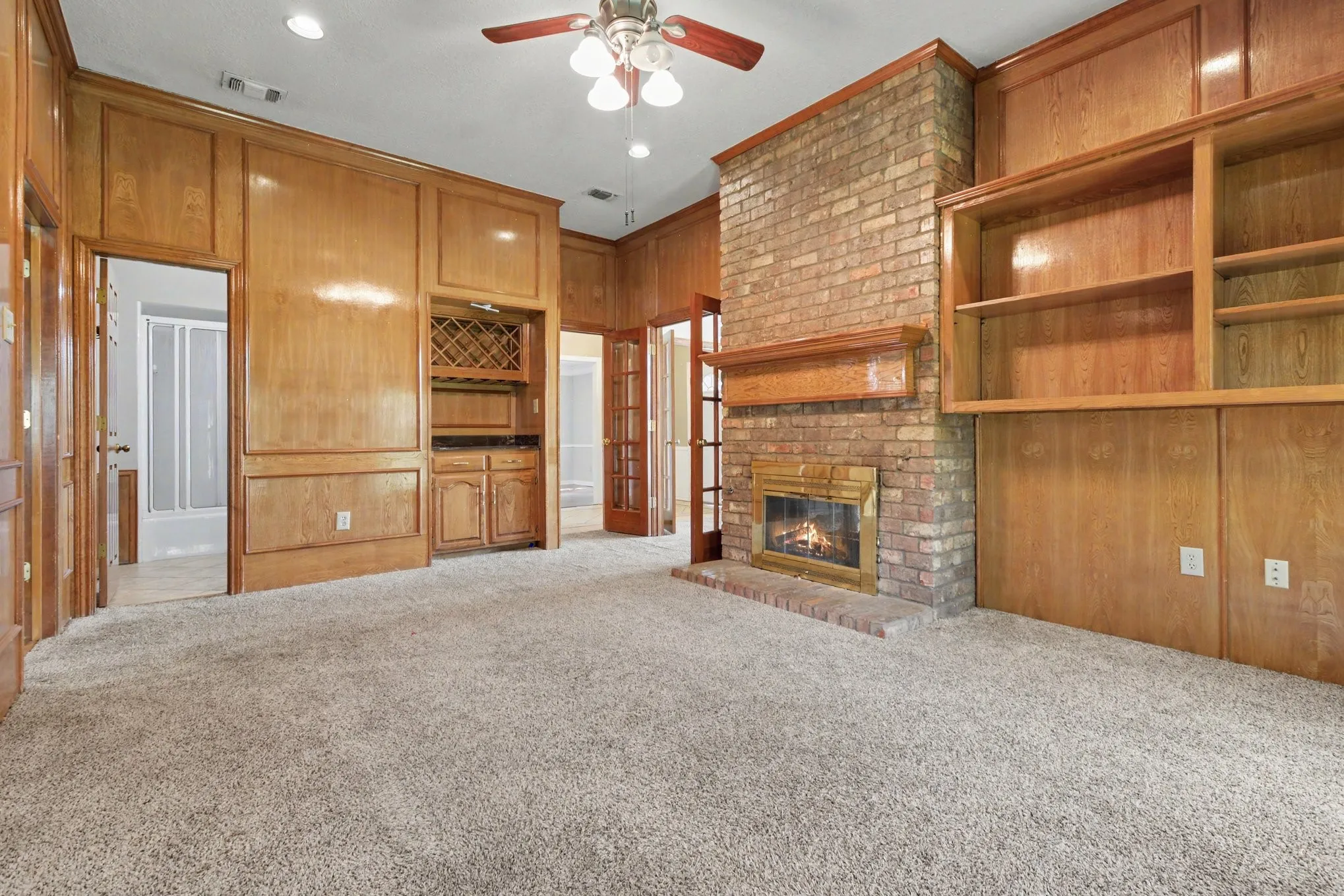 Wood paneling throughout, brick fireplace with mantel, built-in shelving, built-in cabinetry with wine rack, and recessed lighting