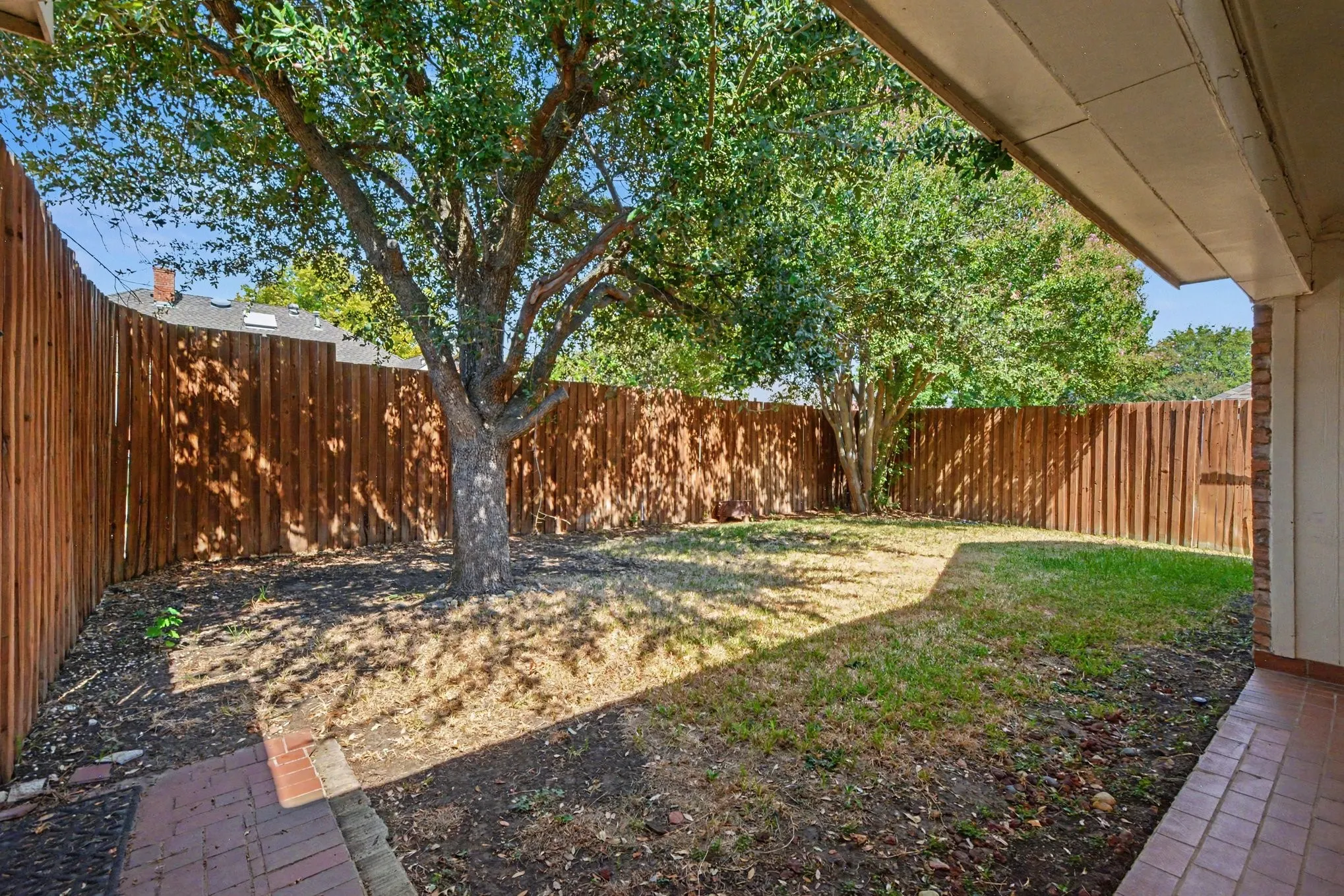 Expansive outdoor space featuring a wood fence, mature tree, brick patio, and green lawn