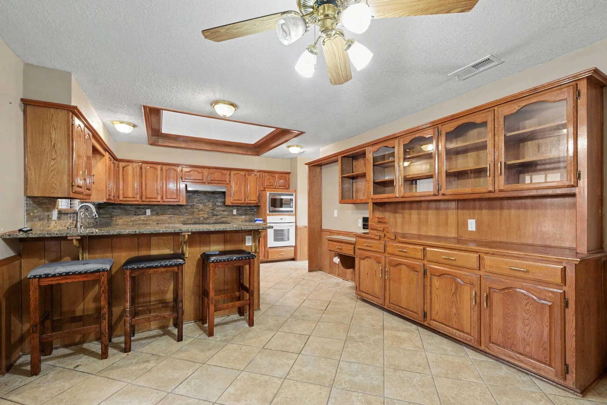 Kitchen featuring extensive wood cabinetry, tile flooring, built-in double oven, built-in microwave, and a ceiling fan