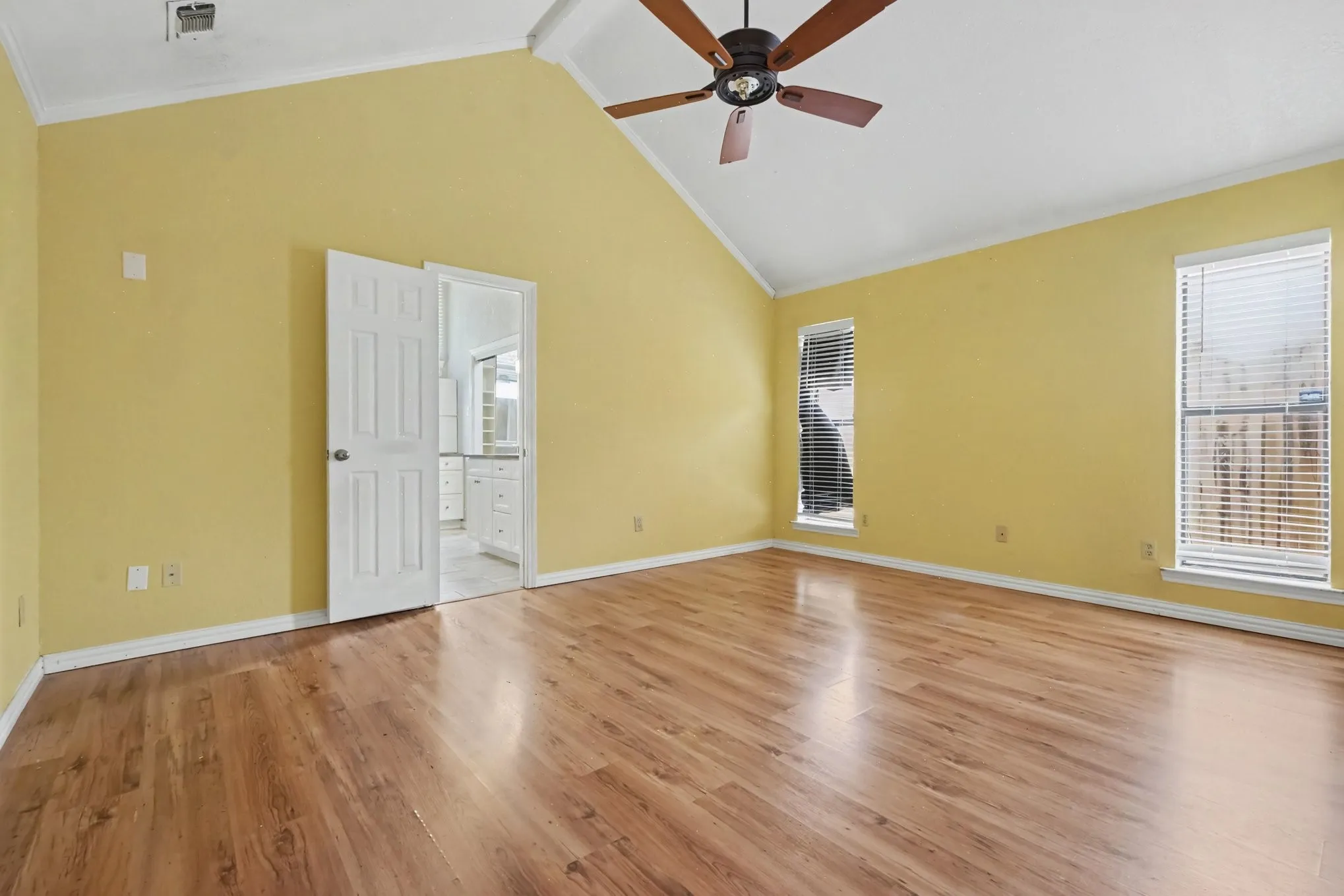 Vaulted ceiling, wood-finish flooring, two windows with blinds, ceiling fan, and white trim