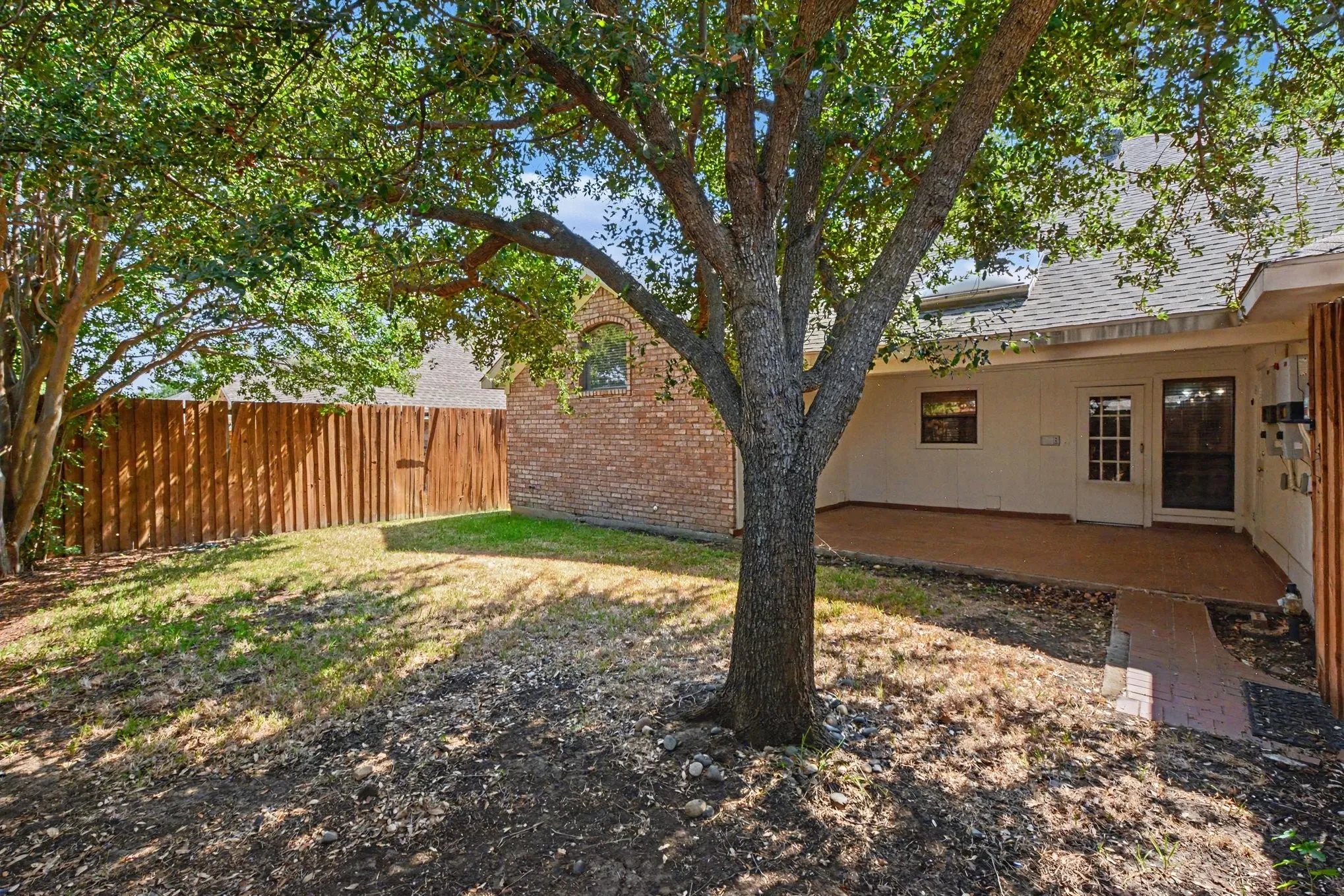 Private backyard space with mature trees, a wooden privacy fence, a covered patio, and a brick pathway