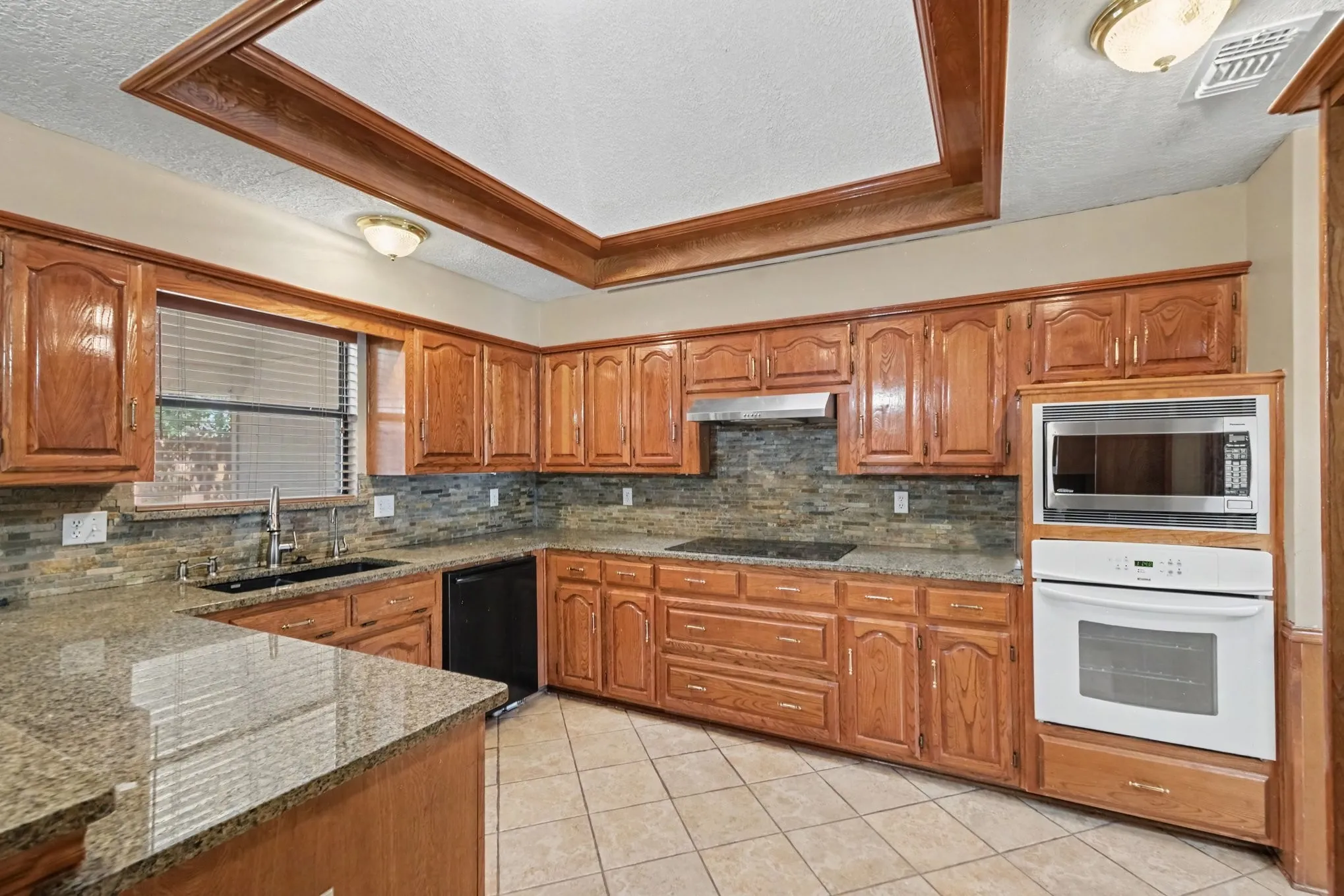 Kitchen featuring wood cabinetry, built-in oven, built-in microwave, stone countertops, and tile flooring