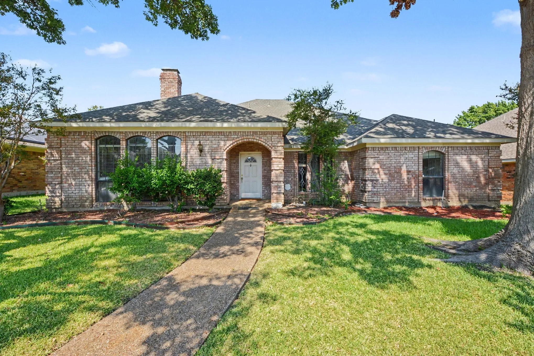 Brick exterior with arched entry, arched windows, a single chimney, and a paved walkway