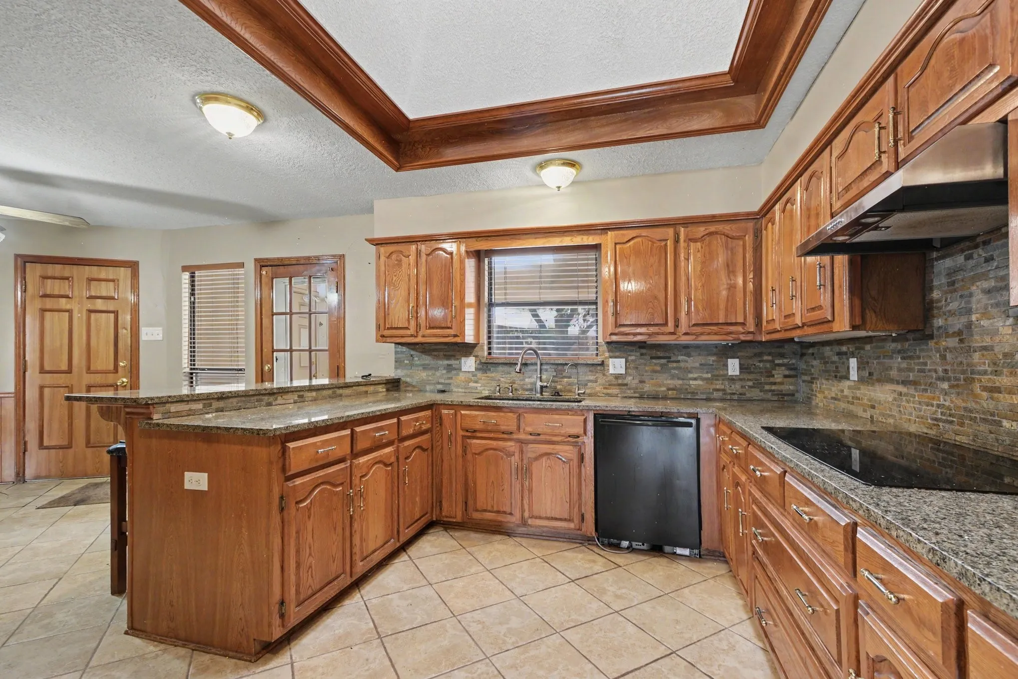 Kitchen featuring wood cabinetry, stone countertops, a tile backsplash, and a coffered ceiling with wood trim