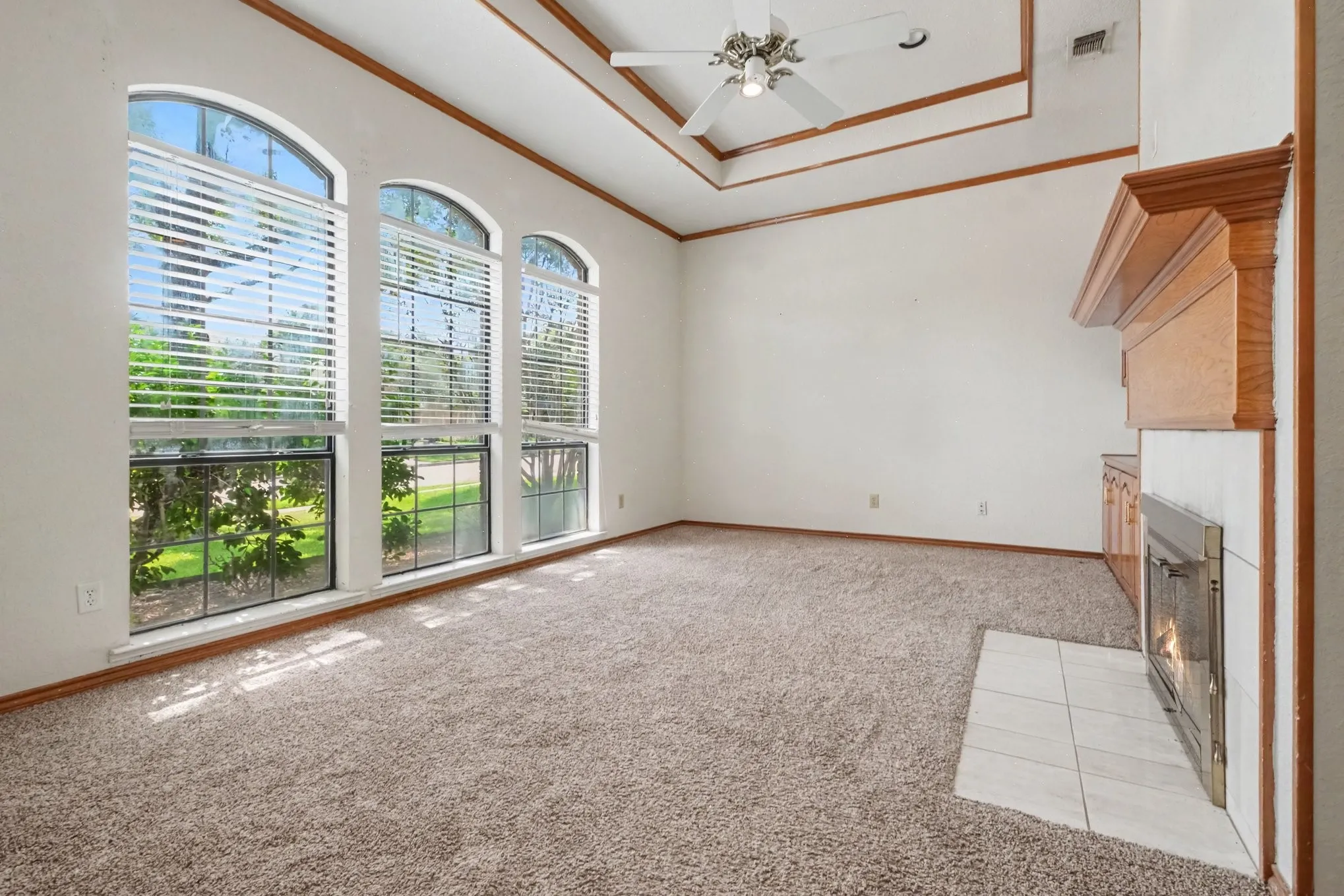 Spacious room featuring three arched windows, a tray ceiling, and a fireplace with a wood mantel