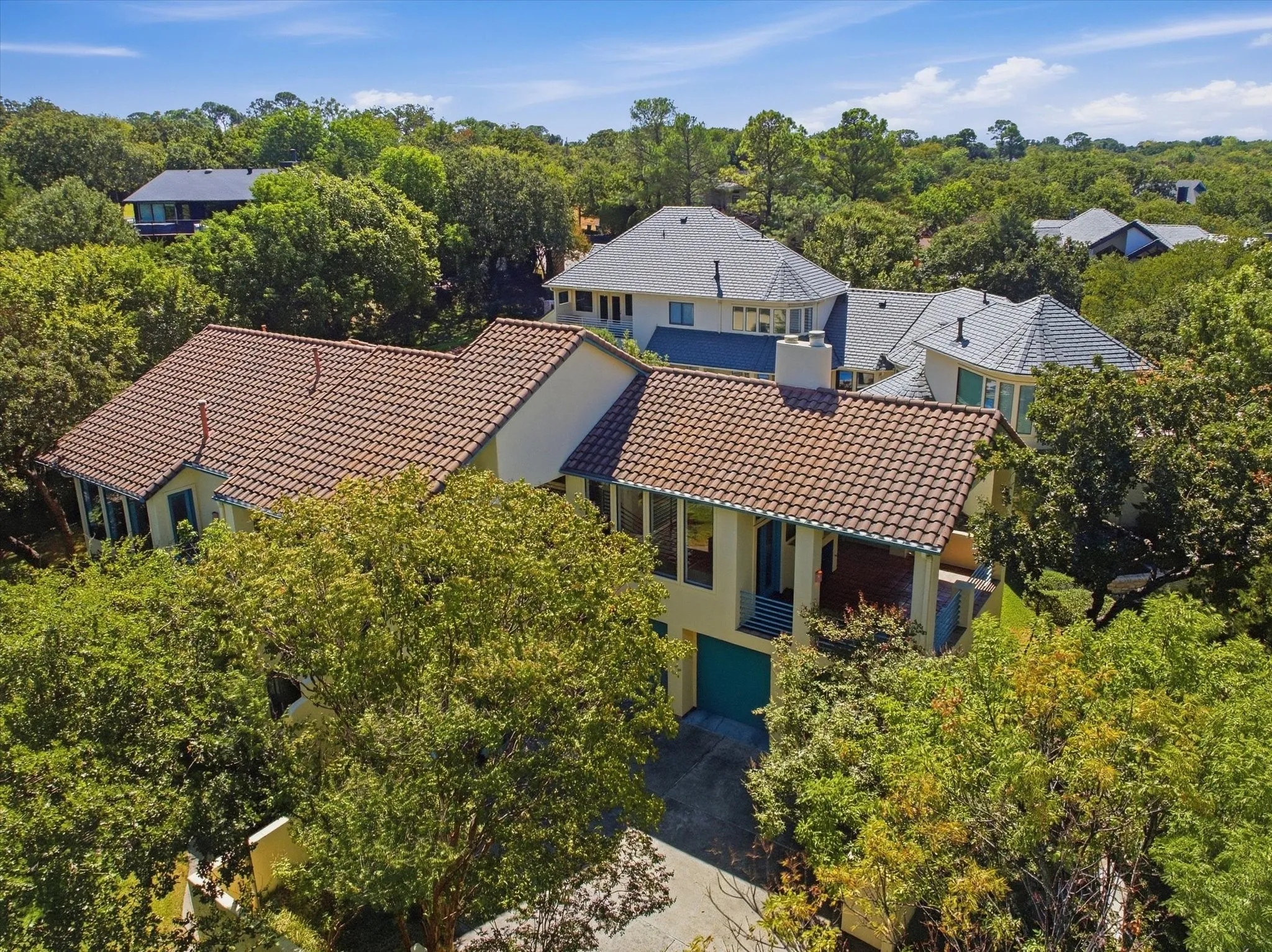 Terracotta tile roof, stucco exterior, multiple large windows, integrated garage, and lush surrounding foliage