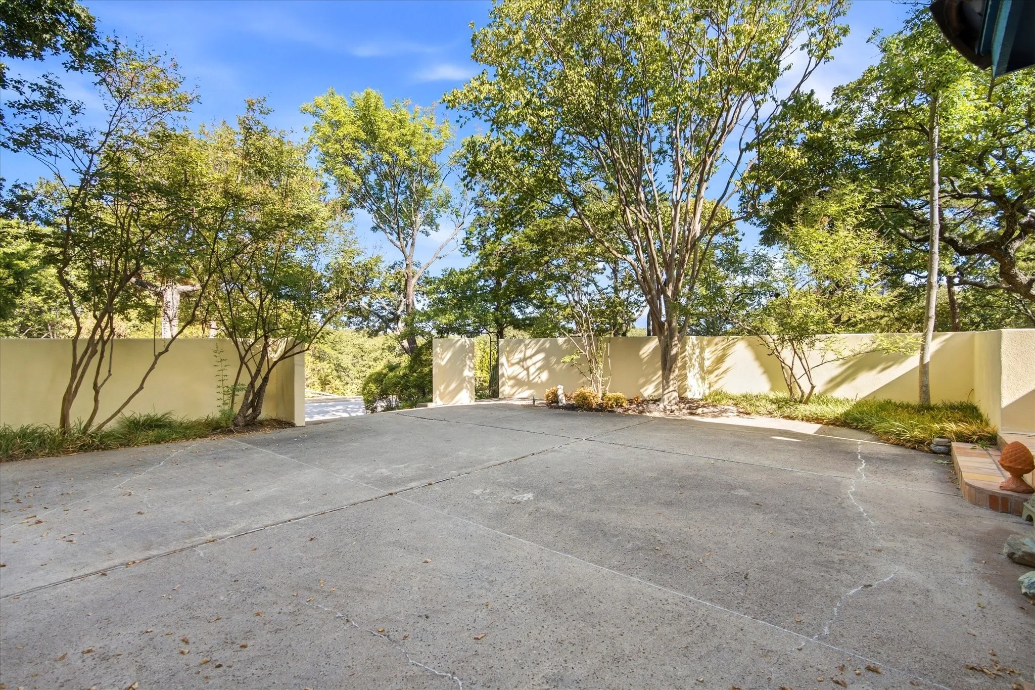 Expansive paved driveway bordered by mature trees and a stucco wall